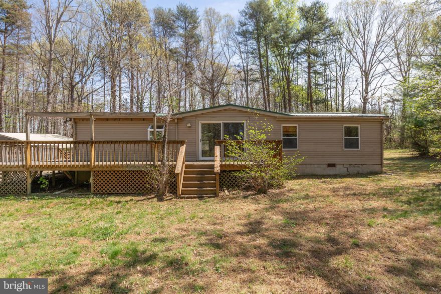 Nestled on over 7 tranquil acres in the heart of Spotsylvania County, this manufactured home offers a unique opportunity to create your vision. Being sold *as is, where is*, this property is ready for updates and improvements—or provides the perfect setting to build your dream home from the ground up.

Tucked toward the back of the lot, the home is accessed by a long, meandering driveway that enhances the sense of privacy and seclusion. The partially wooded acreage offers plenty of space to explore, relax, and enjoy the peaceful surroundings.

Several outbuildings, including carports and sheds, provide ample storage and functionality. Notable updates include a newer standing seam metal roof and HVAC system, offering a strong starting point for future improvements. Foundation work has also been completed for HUD conformance.

A wraparound deck welcomes you and leads to a convenient side entrance through the laundry room. Inside, the centrally located kitchen features table space by a window, along with a separate dining room, den, and spacious family room with a wood-burning fireplace—creating a comfortable hub for gathering.

The primary bedroom includes an attached bath and closet. The second bedroom features a toilet and sink area that will need to be enclosed for privacy.

Bring your ideas and imagination—this property is full of potential and ready to be transformed into something special.

*Acreage and ages of systems are are approximate. Foundation letter confirming HUD compliance is available in the agent documents.*