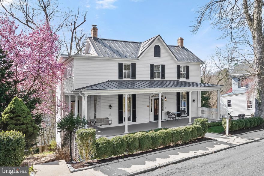 Prepare to fall in love with this charming four bedroom, three full and one half bathroom home in the heart of Old Ellicott City. Built in 1872, this extraordinary home seamlessly blends the original features with luxurious modern amenities. As you arrive, the covered wrap-around front porch greets you and is the perfect spot for enjoying a morning cup of coffee on the swing or watching passerby. Step inside to the foyer that showcases the refinished original oak flooring that continues through the main level. Highlighting an abundance of natural light throughout with floor to ceiling windows, a serene color palette, tall nine foot ceilings, and ornate millwork including dentil crown molding, chair railing, and wainscotting. The front living room features a decorative fireplace and a vintage built-in closet for storage. Off the foyer, double French doors lead to the dining room with a custom wood mantel, and the original pocket doors connect to the family room, offering flexibility while hosting gatherings. The family room also has glass double doors opening onto the wraparound porch, seamlessly blending indoor and outdoor living. Create your chef-inspired meals in the eat-in kitchen with stainless steel appliances, granite counters, recessed lighting, engineered maple wood floors, a built-in corner curio cabinet and space for a breakfast table. An oversized picture window in the kitchen overlooks Old Ellicott City with unparalleled views. The main level also hosts a laundry room,  a walk-in pantry and half bath with marble flooring. Upstairs, a stained glass light illuminates the regal staircase and refinished original heart pine floors adorn the bedrooms. The primary bedroom is a light-filled retreat and the primary bathroom has a walk-in shower. The second bedroom includes an almost soundproof sitting room with a vaulted ceiling - perfect for a cozy nook or office. The third bedroom boasts a decorative fireplace and stained glass hanging light fixture. Down the hall, the second full bathroom has a jetted soaking tub, and around the corner the walk-in dressing room closet offers tons of storage. Downstairs, the walk-out lower level is ideal for a separate living suite with the fourth bedroom and adjacent full bathroom. The bonus room is a versatile area with a walk-in storage closet and the recreation room also is another space for everyone to spread out. A covered balcony provides the perfect spot to unwind and the  exceptional grounds are complete with stone retaining walls, landscaping with flowering trees, a stone patio, and tons of yard space backing to trees. Enjoy living in Old Ellicott City, overlooking Main Street, the Patapsco River and passing trains. Just down the street with pedestrian-friendly access to Main Street for drinks, dining, shopping, exploring and events such as outdoor movie nights and festivals. This coveted home is even included on multiple murals on Main Street and is featured in some of the museums. Located around the corner from the trolley trail for enjoying the serene nature around you with the nearby Roger Carter Community Center. Guaranteed easy parking with a  two-car detached garage with electric, and a driveway - also plenty of street parking. New dishwasher in 2024, air conditioning unit in 2022, radiator covers and custom window treatments 2021. Energy-efficient zoned heating and cooling systems (Central AC) with programmable smart thermostats. Hot water radiators service the main and upper levels.  Newer metal roof, gutters and downspouts installed in 2016, along with new custom milled hardwood cypress siding. With its blend of historic charm and modern updates, this home offers a truly unique opportunity to live in Old Ellicott City. Due to a Historic Preservation Tax Credit that was received several years ago, 3 years of tax credits (towards the county portion of the property tax bill) remain!