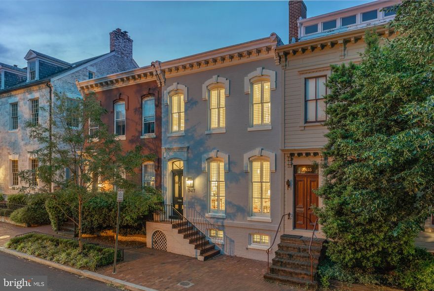 3417 Prospect is a classic townhome comprehensively reimagined, it epitomizes the blend between historic character and contemporary livability. The traditional brick exterior has been repainted a modern gray, contrasting white moldings and the dark stained entry door to create an elegant curb appeal. Inside, the formal living and dining rooms run alongside the foyer and main staircase. Each features a new gas fireplace and mantle; the former’s plantation shutters open to reveal the full-length windows overlooking the streetscape, while the latter custom built-ins, twinkling chandelier and room for 10 make it the ideal place for dinner gatherings. Directly adjoining the dining room is the chef’s kitchen, whose new farmhouse sink, fixtures, lighting, and thick quartz countertops complements commercial SubZero and Wolf appliances. 
The cozy family room enables indoor/outdoor living via French doors which bring the outside in. High ceilings and dark floors throughout the main level convey a sense of spacious sophistication, and a newly added powder room completes the picture. The upper level primary suite overlooks Prospect Street. Its subtly elegant recessed lighting and flush wall of closets are both subtly integrated, while hidden double doors reveal the marble-clad ensuite with dual vanities and glass shower. Two additional bedrooms on the upper level offer similar amenities and share a newly renovated hall bath. The newly dug out lower level, with two additional feet of ceiling height, has its own family room, a fourth bedroom, a stylish full bath with steam shower, and additional storage. It spans 665 square feet of additional living space and substantially augments the home’s functionality. Improvements go beyond skin deep, with new utilities including electrical panel, HVAC, tankless water, and an outdoor irrigation system. The irrigation system services the spectacular rear private and patio.  The deep lot offers outdoor space that is a blend of artful landscaping and extensive hardscaping with lighted brick and flagstone patios enabling seamless al fresco entertaining, a mission furthered by the fire pit and outdoor grill. An oversize detached garage and surface space represents a rarity in the city and completes the home. A masterclass in blending style with livability in an unparalleled location, 3417 Prospect Street NW is a poster child for the modern Georgetown.