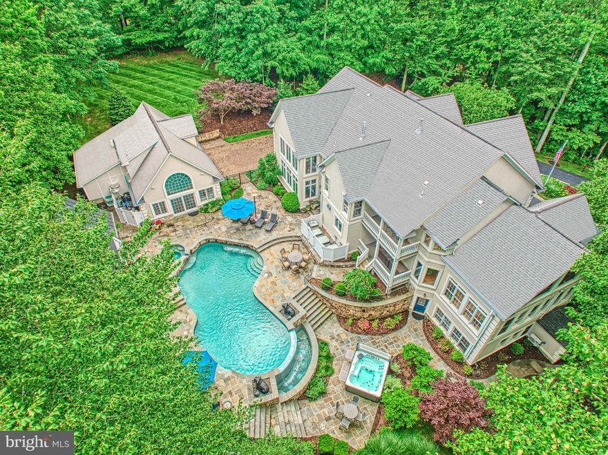 Tucked into more than five acres of wooded privacy, this exceptional residence invites you into a world of elegance, calm, and connection—with nature, with loved ones, and with home. From the moment you turn onto the tree-lined driveway, you’re transported. What unfolds beyond the trees is not just a home, but an experience—a seamless blend of refined living and resort-style amenities, thoughtfully designed for gathering, relaxing, and celebrating life.

Inside, the home opens with timeless warmth. The foyer flows effortlessly to formal living and dining spaces, where a dual-sided fireplace connects to a richly appointed home office—complete with a lofted library accessed by a wrought iron spiral staircase. Anchored by a chef’s dream kitchen, the heart of the home is both functional and beautiful. Custom Amish-built cabinetry, top-tier appliances, leathered quartz surfaces, and a stunning butcher block island come together beneath designer lighting and clever built-ins that maximize both utility and ambiance. A sleek butler’s pantry links the dining room and kitchen, complete with a beverage station and additional prep space.

Adjacent, the great room soars with beam-accented ceilings and a floor-to-ceiling stone fireplace, while diagonally laid wide-plank hardwoods add warmth and movement. The main level also features a well-appointed guest suite, ideal for visitors or multigenerational living.

Upstairs, the primary suite is a peaceful retreat with a cozy fireplace, private balcony access overlooking your home-Oasis, whisper-quiet motorized shades and a spa-inspired bath with custom cabinetry, quartz counters, and a rejuvenating shower panel. Three additional bedrooms each enjoy private en-suite baths, and a reimagined laundry room blends style with efficiency—complete with pet crates, basket cubbies, and granite worktops.

The walkout lower level is an entertainer’s playground: a custom bar with black leathered granite, kegerator, and multiple beverage stations sets the stage for movie nights or game days. A separate craft room with glass French doors and built-in shelving offers creative sanctuary, while the home gym provides daily wellness inspiration.

Step outside, and the magic truly expands. The pool and spa have been reimagined with flagstone, porcelain tile, and smart automation. Nearby, a freestanding hot tub offers additional relaxation. The koi pond has been lovingly restored and now sparkles with life, framed by vibrant landscape design featuring maples, redbuds, and flowering trees. Beyond, the outdoor pavilion is its own destination: over 1,000 square feet of vaulted, covered living and dining space with a full Viking outdoor kitchen, bar seating, stone fireplace, cherry wood ceilings, Big Air wet rated ceiling fans, and curated lighting to extend your evenings under the stars.

The beautifully finished pool house doubles as a guest cottage with its own kitchen, private HVAC system, luxury vinyl plank flooring, and epoxied garage flooring. A newly constructed 24'x14' shed offers elegant functionality with custom storage. The carriage house—part of the eight total garage bays—offers expansive attic storage with pull-down access.

Extensive hardscape and professional landscaping unify the property into a living, breathing retreat. Every element—from the asphalt drive and irrigation systems to the lighting, fencing, and flagstone walkways—has been considered, crafted, and curated.

This isn’t just a property—it’s a personal sanctuary designed to support the full rhythm of life: quiet mornings, lively celebrations, restful evenings, and the beauty of everyday living. Come experience a home that lives as beautifully as it looks.