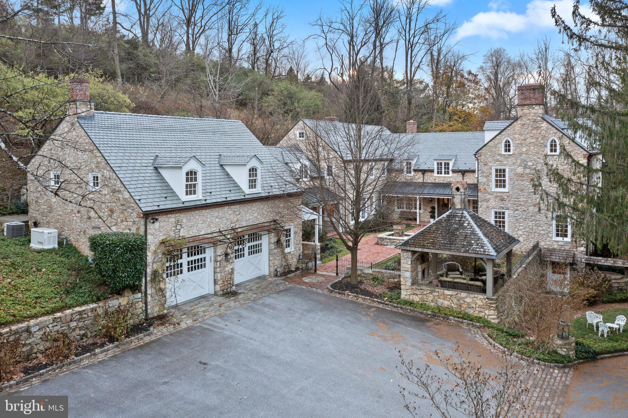 Unbelievable combination of old and new! (This listing is reflected in mls twice to capture the 1782 and 2012 wings.) Drive over a gated bridge and back into history, to the days of the American Revolution, when an English-style farmhouse built in 1782 hosted nurses who cared for the wounded at a nearby church. Today, that carefully renovated Colonial-era stone structure comprises one wing of an exceptional 5/6-bedroom , 5-bath home with nearly 7,300 sq. ft. above grade on 5 private, beautifully manicured acres abutting Valley Creek and Cedar Hollow Natural Preserves Conservancy and Trail in Tredyffrin Township.
Designed by Period Architecture, Ltd., of Malvern, a substantial 2012 addition was built by expert craftsman and Hungarian stone mason Otto Honyak, the previous owner, to form the home’s center and left wings. All stone for the project came from the property, known as Cold Springs Farm.
Step through the oak and leaded glass front door into a harmonious blend of period details, organic materials and modern conveniences. You’ll find 20-in.-thick stone walls, extensive stonework throughout, hand-hewn salvaged timber beams, and custom wrought-iron hardware and light fixtures. Curved walls and arched doorways all call to mind another time, while radiant heated floors, upgraded LED lighting, whole-house generator and security system, 11 woodburning fireplaces (most plumbed for conversion to gas) are among the amenities for today’s lifestyle.
Fully renovated in 2012, the original wing houses a spacious formal dining room and a library/billiards room, w/ random-width knotty oak floors, a powder room, and a 1,100+ sq. ft. walk-out lower-level bonus room w/ fireplace, marble floor and brick-veneered ceiling.
The newer center and left wings, completed in 2012, carry the detailing forward. They house the living room, w/ glass doors leading to a slate patio, and family room, which features soaring beamed ceilings, 2-story stone mantel and glass doors to the patio and fenced in yard. In the period-inspired state-of-the-art kitchen, stone walls and a large stone-and-tile hearth, a fireplace, beamed ceiling and arched doorways, w/ a mix of tile, wood and brick flooring create ambience, while 2 stainless steel Wolf ovens, a Sub-Zero refrigerator, pizza oven, LED lighting and gas cooking add contemporary convenience. The large center island has a farmhouse sink, wooden butcher block and quartz countertops. The kitchen area includes a “keeping room” sitting area, a breakfast nook, a walk-in pantry and access to the mudroom and climate-controlled wine cellar. Windows overlook the courtyard.
Front and back stairs lead upstairs. Behind a rustic wooden door, the private primary bedroom suite in the original wing features a vaulted, beamed ceiling and fireplace, and a loft. The sumptuous ensuite bath has a walk-in closet, built-in burled wood cabinets, a 6x6-ft. glass steam shower. Stone stairs lead to a large jetted soaking tub above the shower, w/ an additional fireplace for the ultimate in relaxation. Across the landing, in the addition, 2 bedrooms have walk-in closets and ensuite baths, a 3rd has an ensuite bath, a walk-in closet and adjoining bonus room w/ vaulted ceiling, which is currently used as a 6th bedroom. Laundry room in hall.
Above the attached 2-car garage is a 1 bed/1 bath apartment w/ a kitchen and an open-concept room. The property also includes a 2-story mid-19th-century barn, fully renovated w/ steel beams and concrete in 2012, w/ 3 garage bays and a rear upper-level entrance. A rustic 2-story “entertainment cabin” built in 2012 has a fireplace on each level.
A brick-paved courtyard and garden w/ fountain and wrought-iron fencing, a stone gazebo w/ fireplace and a pond adorn the grounds.
Centrally located 3.7 miles to Paoli train station that Acela services, approx. 1 mile to PA Turnpike and 202 w/ access to 76/476, 40 minutes to Center City and airport, 15 minutes to Wayne.