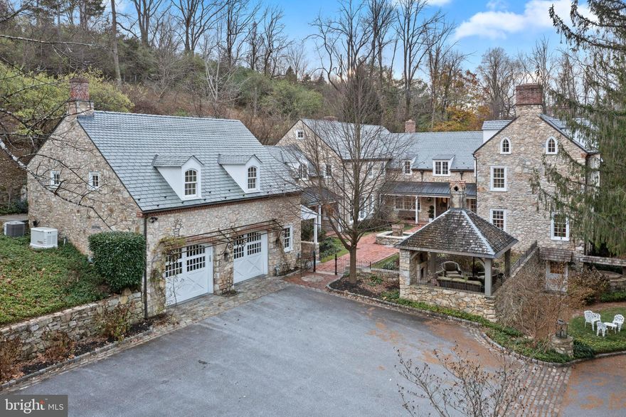 Unbelievable combination of old and new! (This listing is reflected in mls twice to capture the 1782 and 2012 wings.) Drive over a gated bridge and back into history, to the days of the American Revolution, when an English-style farmhouse built in 1782 hosted nurses who cared for the wounded at a nearby church. Today, that carefully renovated Colonial-era stone structure comprises one wing of an exceptional 5/6-bedroom , 5-bath home with nearly 7,300 sq. ft. above grade on 5 private, beautifully manicured acres abutting Valley Creek and Cedar Hollow Natural Preserves Conservancy and Trail in Tredyffrin Township.
Designed by Period Architecture, Ltd., of Malvern, a substantial 2012 addition was built by expert craftsman and Hungarian stone mason Otto Honyak, the previous owner, to form the home’s center and left wings. All stone for the project came from the property, known as Cold Springs Farm.
Step through the oak and leaded glass front door into a harmonious blend of period details, organic materials and modern conveniences. You’ll find 20-in.-thick stone walls, extensive stonework throughout, hand-hewn salvaged timber beams, and custom wrought-iron hardware and light fixtures. Curved walls and arched doorways all call to mind another time, while radiant heated floors, upgraded LED lighting, whole-house generator and security system, 11 woodburning fireplaces (most plumbed for conversion to gas) are among the amenities for today’s lifestyle.
Fully renovated in 2012, the original wing houses a spacious formal dining room and a library/billiards room,  w/ random-width knotty oak floors,  a powder room, and a 1,100+ sq. ft. walk-out lower-level bonus room w/ fireplace, marble floor and brick-veneered ceiling.
The newer center and left wings, completed in 2012, carry the detailing forward. They house the living room, w/  glass doors leading to a slate patio, and family room, which features soaring beamed ceilings,  2-story stone mantel and  glass doors to the  patio and fenced in yard. In the period-inspired state-of-the-art kitchen, stone walls and a large stone-and-tile hearth, a fireplace, beamed ceiling and arched doorways, w/ a mix of tile, wood and brick flooring create ambience, while 2 stainless steel Wolf ovens, a Sub-Zero refrigerator, pizza oven, LED lighting and gas cooking add contemporary convenience. The large center island has a farmhouse sink, wooden butcher block and quartz countertops. The kitchen area includes a “keeping room” sitting area, a breakfast nook, a walk-in pantry and access to the mudroom and climate-controlled wine cellar. Windows overlook the  courtyard.
Front and back stairs lead upstairs. Behind a rustic wooden door, the private primary bedroom suite in the original wing features a vaulted, beamed ceiling and fireplace, and a loft. The sumptuous ensuite bath has a walk-in closet,  built-in burled wood cabinets, a 6x6-ft. glass steam shower. Stone stairs lead to a large jetted soaking tub above the shower, w/ an additional fireplace for the ultimate in relaxation. Across the landing, in the addition, 2 bedrooms have walk-in closets and ensuite baths, a 3rd has an ensuite bath, a walk-in closet and adjoining bonus room w/ vaulted ceiling, which is currently used as a 6th bedroom. Laundry room in hall.
Above the attached 2-car garage is a 1 bed/1 bath  apartment w/ a kitchen and an open-concept room. The property also includes a 2-story mid-19th-century barn, fully renovated w/ steel beams and concrete in 2012, w/ 3 garage bays and a rear upper-level entrance.  A rustic 2-story “entertainment cabin” built in 2012 has a fireplace on each level.
A brick-paved courtyard and garden w/ fountain and wrought-iron fencing,  a stone gazebo w/ fireplace and a pond adorn the grounds.
Centrally located 3.7 miles to Paoli train station that Acela services, approx. 1 mile to PA Turnpike and 202 w/ access to 76/476,  40 minutes to Center City and airport, 15 minutes to Wayne.