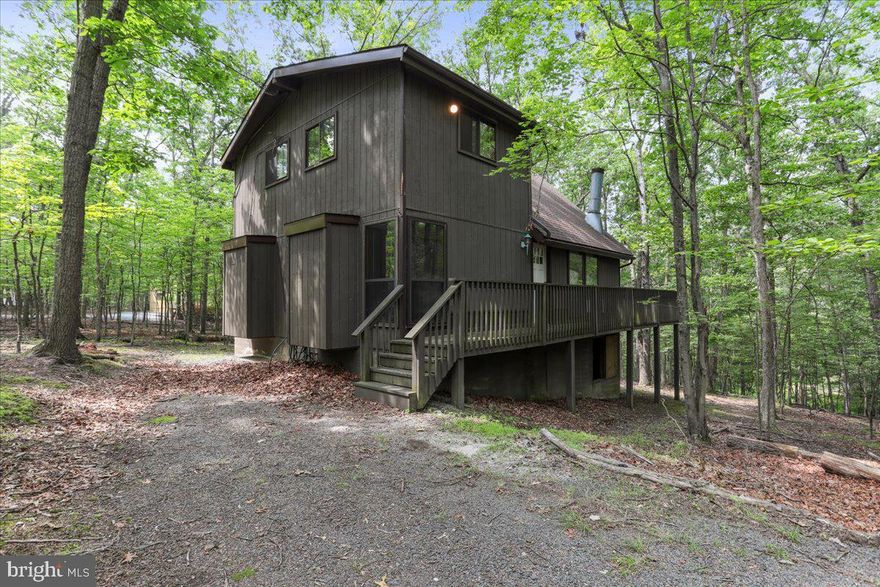 Set on a tranquil, wooded lot in the Walden Woods section of The Woods Resort community, 772 Walden Rd is a spacious 3-bedroom, 2-bath home offering over 1,800 square feet of comfortable living space with a flexible layout designed to embrace its natural surroundings.

The main level features a bright and open great room with vaulted ceilings, a wood-burning stove, and a wall of windows that frame the peaceful outdoor views. The adjoining dining area is perfect for everyday meals or entertaining, with seamless access to the rear deck for extended living space. This level also includes two well-proportioned bedrooms and a full bath, offering convenience and flexibility for guests or family members.

Upstairs, a loft space overlooks the great room below and provides the perfect spot for a home office or reading nook. Just beyond, the private primary suite serves as a peaceful retreat, complete with its own full bath and tree-lined views.

Enjoy outdoor living on the expansive rear deck, surrounded by mature trees and backing to protected woodland—offering both privacy and year-round natural beauty. Additional features include a full-size laundry area and a generous driveway with space for multiple vehicles.

Located within The Woods Resort, residents enjoy access to walking trails, indoor and outdoor pools, tennis courts, a fitness center, clubhouse, golf course, and a stocked fishing pond. Optional memberships are available for expanded use of resort amenities, including spa services and event spaces.

Situated just 20 minutes from Martinsburg and under 2 hours from Washington, D.C., the location provides the perfect balance of quiet, resort-style living with easy access to shopping, dining, and commuter routes. Nearby attractions include Cacapon Resort State Park, Sleepy Creek Wildlife Management Area, and the charming shops of historic Berkeley Springs.

772 Walden Rd is ideal for those seeking a full-time home or a relaxing weekend getaway in a vibrant, amenity-rich mountain community.