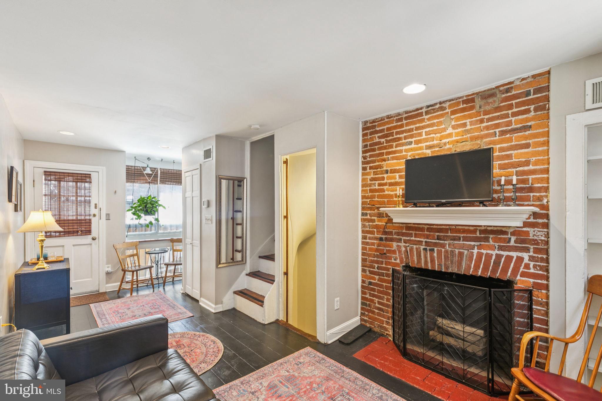 Planned and built in the Georgian style while Thomas Jefferson was still President, this charming, historically certified property is located in the Society Hill Historic Preservation District. Expanded trinity with wood flooring throughout. Full of character on a centrally located, desirable block. The street-entry level features a lovely living room with an exposed brick fireplace, a half bath, a rear two-story window wall currently used as a natural-light indoor garden area with a cozy conversation nook, a coat closet, and access to a brick patio with new fencing. This private outdoor space includes a five-foot-deep Canadian cedar hot tub under a gazebo with side privacy panels, plus a barbecue or garden area. Stairs lead down to a lower-level kitchen with separate street access and a full dining area with a brick fireplace and wood flooring. The second floor has one bedroom with a brick fireplace and wood flooring, as well as a large primary bathroom with a soaking tub, double vanity with granite top and vessel sinks, and a glass block wall that allows for abundant natural light. The third floor features another bedroom with wood flooring and access to a privacy-walled roof terrace—ideal for private sunbathing or moonlit cocktails. The fourth floor is a dormered third bedroom.
One level below the kitchen is an unfinished basement, which includes a massive arched walk-in fireplace—possibly originally used for cooking. New water heater (2020) and roof (2018). Total home warranty until 10/1/26 will be transferred to new buyer!