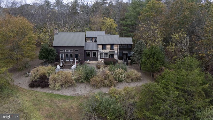 An architectural gem designed by Diane Lohman with input from the sellers. This property features two original log cabins, circa 1800's from Virginia that were dismantled, moved to the current location and put back together with a connecting addition maintaining the authenticity of the time period with a choice of materials to create a wonderful home with all the modern conveniences of today and the feel of yesterday.   We'll try to help you visualize the beauty of this property.
The home is located on 5.4 natural acres in the Ice Mountain subdivision offering a trail to cross the North Branch of the Potomac river via a swinging bridge.  Hike the mountain and enjoy the views of the ridge and algific talus slope that is part of a 149 acre preserve that is designated as a National Natural landmark.  It is nicknamed" Nature's Ice Box" or "Nature's Refrigerator" due to its ice vents that release cool air year round.
Locally sourced cherry hand hewn wood floors , a magnificent stacked stone fireplace with a custom forged iron fireguard, built in bookcases and two single bed size window seats compliment the cozy great room with a door opening onto the rear patio.
The family room, adjacent dining room and kitchen all offer scenic views of the community area "meadow" and Ice Mountain which lies across the river.
The kitchen has custom built cabinets with soapstone sink and fire slate counters, a large island with a propane cooktop with tile floors. Situated off the kitchen is a large open pantry with plenty of storage.  Enjoy the screened porch directly off the kitchen.
There is a large first floor bedroom with connecting bathroom that also serves guests.
The upstairs has two large bedrooms each with a private bath, one with access to a wonderful screened porch that also has a steam shower in the bath.
The  lower level offers another bedroom and private bath, laundry area and utilities room.
The outside offers a lovely stone patio with walkways thru the beautifully maintained gardens.
The whole house generator and Tesla car charger will convey with the sale of the house along with most furnishings.  The furniture deserves its own descriptions , the seller will leave a list of the pieces and 
history of each.