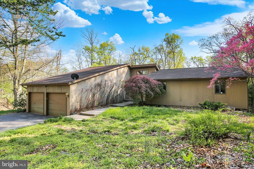 Nestled on Ridge Road in a serene semi-rural setting, this striking mid-century modern residence is surrounded by mature trees, rolling hills, and sweeping natural views across its private 4-acre lot. Offering a rare blend of privacy, space, and architectural character, the home is filled with natural light and thoughtfully designed living areas.
A two-story foyer welcomes you into the heart of the home, where soaring ceilings extend through the kitchen, dining, and living spaces. Expansive Andersen casement windows frame the surrounding landscape and bring the outdoors in. The sunken living room features new carpet, a skylight, and a full stone wood-burning fireplace with a built-in bar area—perfect for entertaining or relaxing evenings at home.
The dining room, elevated just steps above, showcases beautiful hardwood flooring and flows seamlessly into the kitchen. The kitchen offers granite countertops, a copper double sink, and a highly functional cabinetry layout with excellent storage. With a bit of finishing touch, the space has the potential to truly shine.
The main level includes three bedrooms with new carpeting throughout. The spacious primary suite features a large walk-in closet and a newly built tiled shower with skylight, creating a bright and private retreat. A convenient first-floor laundry adds everyday ease. One of the home’s standout features is the lower-level exceptional versatility with a fully functional in-law suite, complete with a kitchen, family room, bedroom, full bath, separate laundry, independent electrical panel, and private exterior entry—ideal for multigenerational living or potential rental income. An additional unfinished lower-level family room includes a second stone wood-burning fireplace and walk-out access to a large rear patio.
The expansive wraparound rear deck, accessible from the primary bedroom, living room, and dining room overlooks the wooded backyard, it provides a peaceful vantage point for wildlife viewing, morning coffee, or evening gatherings. A brand-new HVAC system installed in late 2025 adds modern comfort and peace of mind.
A two-car garage provides additional storage space. This estate sale presents a unique opportunity to build equity in a home with strong bones, character, and incredible potential. While some cosmetic updates are needed—including select trim work, kitchen finishing details, and deck repairs—the property is priced to reflect its current condition and invites a buyer ready to make it their own.