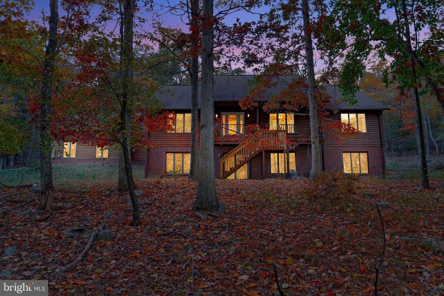 Beautifully maintained custom-built brick and cedar-sided mountain getaway on more than four acres! This 2,100-square-foot home boasts 3 bedrooms, 2 baths, a study, formal dining room, and beautiful open-concept living room-kitchen area. Hardwood floors, ceramic tile, and berber carpet throughout. Relax in front of the wood-burning fireplace and watch the wildlife through handsome picture windows. Deer and wild turkey are frequent visitors. Year-round spring on property. Rear patio equipped to accomodate hot tub. 240-Amp Service. ADA Compliant. HVAC, with remote programmable thermostat, replaced within past 8 years. Full unfinished basement equipped for future bathroom and wood burning stove. Gravity-fed septic. Hybrid Heat Pump-Propane combo heating system with privately-owned propane tank. Back-up septic installed for future use. This beautifully-maintained second home is 20 years old but shows like new! Cedar has been stained and sealed every 5 years. Dish satellite internet onsite. Two-car garage and spacious gravel drive offer plenty of room for parking. Furnishings are available for purchase separately. Annual memberships can be purchased for access to adjacent Avalon Resort, which features vacation condos, lodge, and an aquatics center. Just two hours from DC area, 40 minutes from fabulous shopping and restaurants in Winchester, VA, and 30 minutes to the historic spas of Berkeley Springs, WV. This home is part of a family-friendly clothing optional community. Come check out this unique property on Pendragon Court and find out precisely why West Virginia is considered "Almost Heaven."