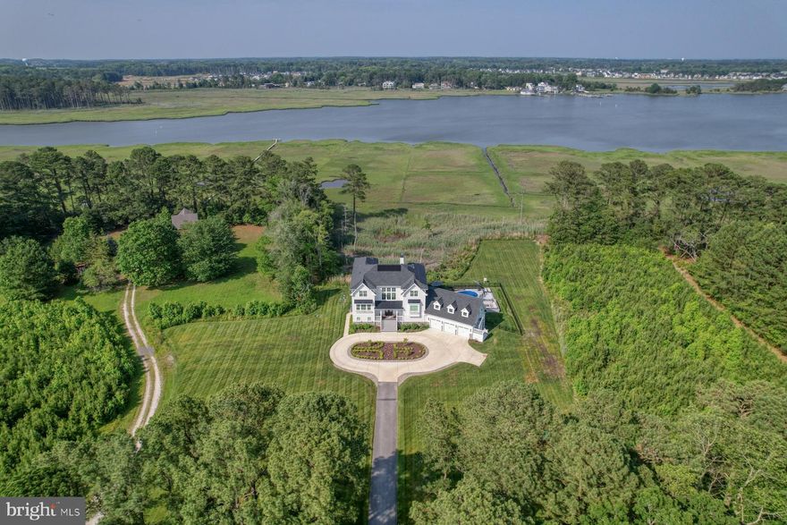 Spectacular Private Waterfront Estate on Love Creek!  A rare opportunity to own a stunning custom-built waterfront retreat nestled on 6.69 acres along tranquil Love Creek, with direct access to Rehoboth Bay. This exquisite property offers 6,840 square feet of heated living space (8,509 total) and includes a boat slip, making it a perfect sanctuary for nature lovers and water enthusiasts alike.  A long, private drive with a circular turnaround leads to the welcoming front staircase and charming covered porch. Inside, the foyer opens to both the main and ground levels. The heart of the home is the breathtaking two-story great room, featuring a dramatic stone fireplace, a wall of windows, and sliding glass doors showcasing panoramic water views. Step onto the expansive, maintenance-free deck and enjoy gentle bay breezes while watching bald eagles soar overhead.  The gourmet kitchen is a chef’s dream, complete with a large island, quartz countertops, walk-in pantry, high-end stainless steel appliances, tile backsplash, and rich hardwood floors. It flows seamlessly into a bright dining area surrounded by three walls of windows overlooking the water.  The main level also includes a home office with custom built-ins, a stylish powder room, and a luxurious owner’s suite. The primary bedroom features tray ceilings, elegant moldings, wainscoting, serene water views, and dual walk-in closets—one with a built-in makeup vanity, desk, and stackable washer/dryer. The spa-like owner’s bath boasts a clawfoot soaking tub, oversized tile shower, and separate vanities.  The lower level is designed for entertainment and comfort, with a guest bedroom, full bath, wet bar (with pass-through to the screened porch), a spacious family room, media room, and two mudrooms—one equipped with a dog wash station. Walk out to a large screened porch that leads to a resort-style outdoor oasis, complete with a pool, firepit, outdoor kitchen, mistaway system, and a Marmiro marble patio.  Upstairs, the third level features three additional en-suite bedrooms, a loft, and a bonus room with sweeping views. One of the bedrooms offers private deck access—the perfect perch for watching Rehoboth Beach fireworks.  A spacious three-car garage includes a bonus room above with a private staircase, ideal for storage or future living space.  Featuring wide plank hardwood floors, solar panels (owned), custom tile and millwork throughout, elevator shaft for future elevator to all three levels, energy efficient dual fuel hvac, and Rennai hot water on demand.  Room to add a ADU(Accessory Dwelling Unit), pole barn, and potential for acquiring additional acreage.  Convenient to Lewes and Rehoboth attractions by car and boat!  This exceptional estate offers the perfect blend of luxury, privacy, and waterfront living. Hard to reproduce this home and finishes for this price!  Don’t miss the video tour—your dream home awaits!
