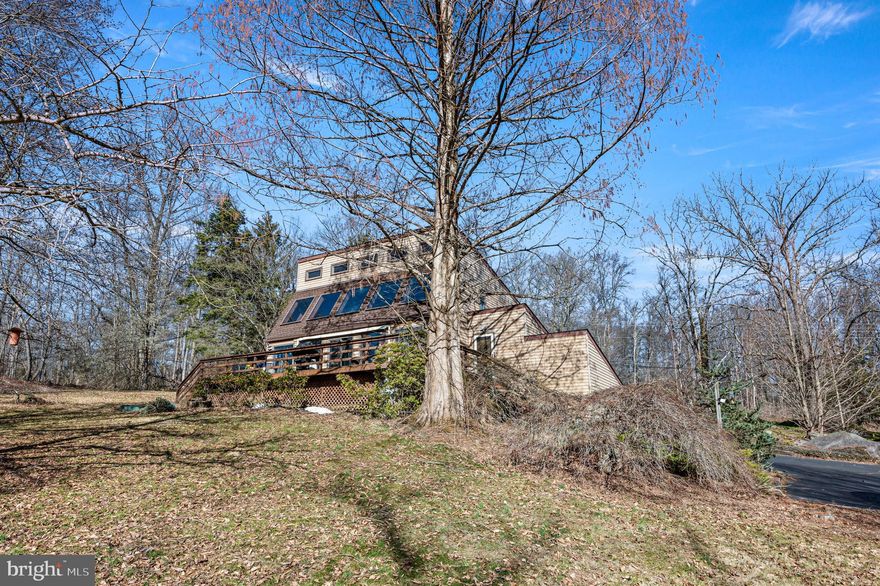 Set on more than 5 beautifully landscaped and wooded acres bordering the Unami Creek, this one-of-a-kind Milford Township property offers a rare combination of privacy, natural beauty, and innovative energy-conscious design. Tucked along a quiet rural road, yet just minutes from Quakertown shopping, restaurants, the PA Turnpike, and Fox Hollow Golf Club, this is a home you truly need to experience in person to appreciate.
Unlike anything else on the market, this 3-bedroom, 2-bath home was designed as a passive solar heat residence, featuring a dramatic two-story solarium along the south wall that helps circulate natural warmth throughout the home. A double-roof and double-wall system, extra-thick insulated east and west walls, and a cast-iron wood-burning stove all contribute to the home's remarkable efficiency and distinctive character. 
Inside, the first floor offers a spacious living room, dining area, full bath with laundry, basement access, and a remodeled kitchen layout that now opens the main living space for a more modern, airy flow. Upstairs, you’ll find three bedrooms and a second full bath, including a primary bedroom with a large walk-in closet and sliding door access to a balcony overlooking the solarium.
The full basement is exceptionally dry and provides abundant storage, shelving, and a water conditioning system. An oversized garage includes a workbench area, an overhead storage, and extensive shelving. Outside, a large deck overlooks the stunning grounds, which were lovingly planted with a wide variety of mature trees and unique specimen plantings, including Redwood trees.