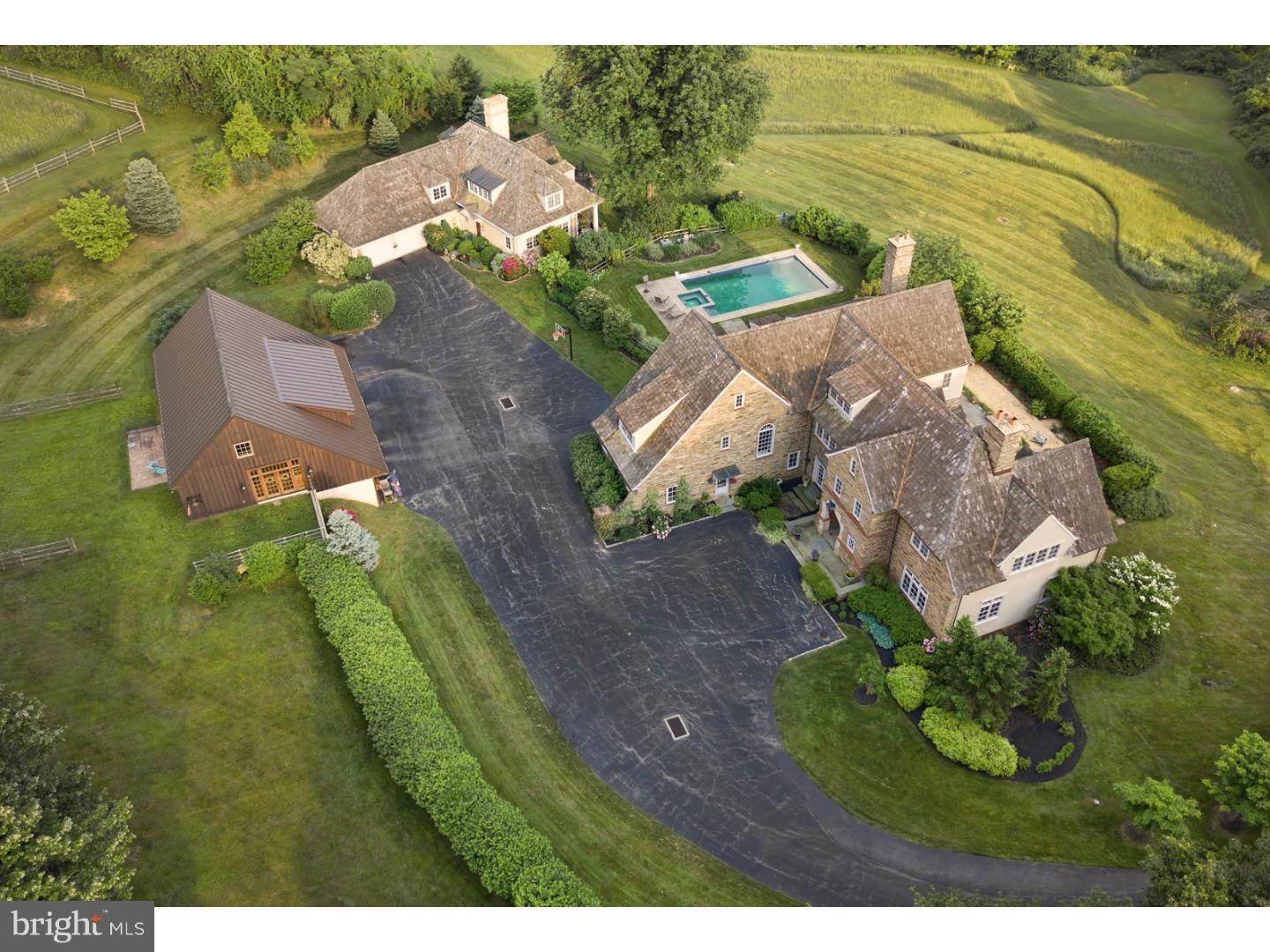 This grand stone estate is located in Villanova's desirable Ardrossan neighborhood, and features 5 bedrooms with 5 full & 3-half baths. Surrounded by over 14 lush acres, the expansive and gorgeous property includes a main home, a guest house and a finished barn. Cathedral ceilings, a dramatic spiral staircase and gleaming hardwood floors are at the centerpiece of this home's light-filled interior foyer. Adjacent is the spacious formal dining room, with outdoor access via French doors. It leads directly into the gourmet kitchen, with custom cream-colored cabinetry, a center island with seating, luxury appliances and plenty of counter-space and cabinets. The kitchen also offers additional seating space. A generously-sized butler's pantry and airy living room with a fireplace are also connected to the kitchen. There is a powder room nearby and the mudroom includes an oversized stationary sink and floor-to-ceiling closets. A lovely and unique brick indoor hallway stretches the length of the home, bringing in light and offering access to the outdoors. Outside of the home features an open terrace in the rear with an ample seating area. Upstairs, the large master suite includes a bathroom with double sinks, and generously-sized shower, soaking tub and plenty of storage. Three additional sizable bedrooms also have their own adjacent bathrooms complete this level. Finished lower level includes wall-to-wall carpeting and built-in bookshelves along one wall, with room for a gym, playroom and other activities. Outside, this home also features beautifully landscaped grounds with an elegant in-ground rectangular swimming pool and a surrounding seating area. Also on-property is the 3-bedroom, 2-full bathroom guest house with dramatic, cathedral ceilings, built-in bookcases and a fireplace in the living room. It features a spacious, modern kitchen, hardwood floors and a two-car attached garage. The second floor features an interior balcony overlooking the first floor's common areas. In addition, the home includes a 2-story finished barn with a contemporary design and an abundance of windows overlooking the surrounding acres. This structure also has a 3-car garage and an expansive and stylish recreation space with the warm embrace of floor-to-ceiling knotty pine that's ideal for guest gatherings. This exceptional and magnificent property is truly a one-of-a-kind treasure!