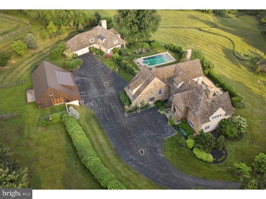 This grand stone estate is located in Villanova's desirable Ardrossan neighborhood, and features 5 bedrooms with 5 full & 3-half baths. Surrounded by over 14 lush acres, the expansive and gorgeous property includes a main home, a guest house and a finished barn.  Cathedral ceilings, a dramatic spiral staircase and gleaming hardwood floors are at the centerpiece of this home's light-filled interior foyer. Adjacent is the spacious formal dining room, with outdoor access via French doors. It leads directly into the gourmet kitchen, with custom cream-colored cabinetry, a center island with seating, luxury appliances and plenty of counter-space and cabinets. The kitchen also offers additional seating space. A generously-sized butler's pantry and airy living room with a fireplace are also connected to the kitchen. There is a powder room nearby and the mudroom includes an oversized stationary sink and floor-to-ceiling closets. A lovely and unique brick indoor hallway stretches the length of the home, bringing in light and offering access to the outdoors. Outside of the home features an open terrace in the rear with an ample seating area. Upstairs, the large master suite includes a bathroom with double sinks, and generously-sized shower, soaking tub and plenty of storage. Three additional sizable bedrooms also have their own adjacent bathrooms complete this level. Finished lower level includes wall-to-wall carpeting and built-in bookshelves along one wall, with room for a gym, playroom and other activities. Outside, this home also features beautifully landscaped grounds with an elegant in-ground rectangular swimming pool and a surrounding seating area. Also on-property is the 3-bedroom, 2-full bathroom guest house with dramatic, cathedral ceilings, built-in bookcases and a fireplace in the living room. It features a spacious, modern kitchen, hardwood floors and a two-car attached garage. The second floor features an interior balcony overlooking the first floor's common areas. In addition, the home includes a 2-story finished barn with a contemporary design and an abundance of windows overlooking the surrounding acres. This structure also has a 3-car garage and an expansive and stylish recreation space with the warm embrace of floor-to-ceiling knotty pine that's ideal for guest gatherings. This exceptional and magnificent property is truly a one-of-a-kind treasure!