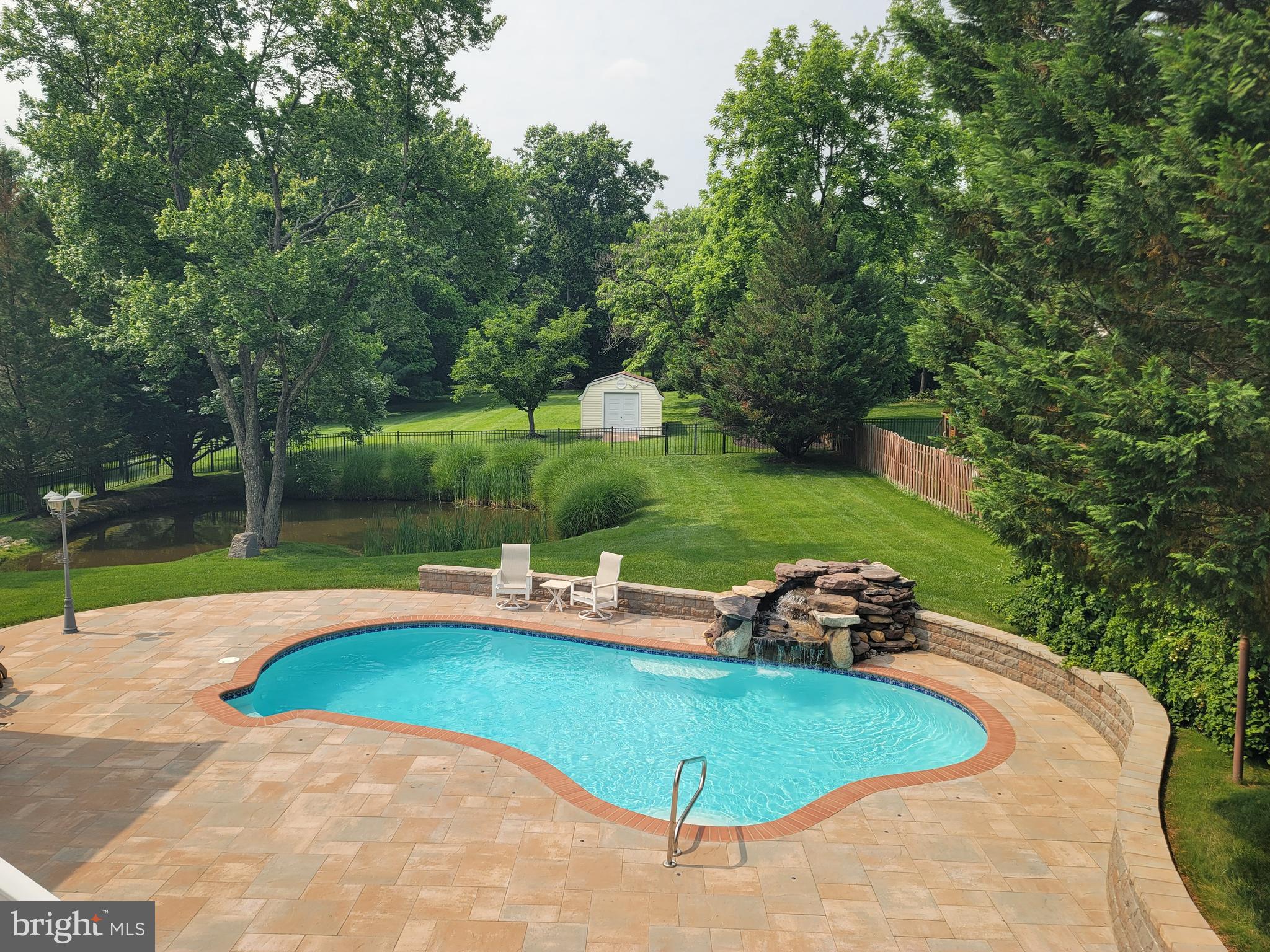A unique custom built home! Brick front transitional rancher with oversized 4 car garage, natural pond with fountain, inground pool with waterfall, on just over 1 acre. Looking for a room with a view? It is hard to pick just one! Almost every room has a unique view of trees and all rear views are water views of the pool and pond. From the front angle you would not expect to find over 4400 sq ft of living space but it's all here. A traditional look from the outside but a modern contemporary floor plan inside. Entering from the covered front porch, the main level features cathedral 2 story ceilings and 2 oversized sliders with transoms. These combine to make for a bright and airy main living space. Formal dining room open to the sunken great room. Double sided gas fireplace shared between the great room and the kitchen. Both great room sliders access the large tiered Trex deck. The 14x26 ft kitchen has a unique box bay table space with built in seating with vaulted ceiling and a picturesque Palladian window looking out to the Ginga tree. Center island with breakfast bar. Granite countertops. Omega solid wood cabinets with pecan finish, under cabinet lighting. Newer appliances including the built-in convection KitchenAid oven, SS Whirlpool Profile refrigerator and KitchenAid SS dishwasher, all less than 1 year old. Double door pantry with wood shelves. Backdoor off the kitchen leads to deck, perfect for grilling. Center of the home has an atrium with another slider access to the deck. There are 3 bedrooms and 2 full baths on the main level including a 22x30 primary suite. Inside the primary suite you will again find the 2 story cathedral ceilings, double sided gas fireplace, and plenty of natural light from all the windows. A sunroom is included inside the suite and features panoramic views from the 3 walls of windows. The generous walk in closet adjoins the primary bath. Separate vanities, expanded tiled shower and whirlpool/ jetted Kohler tub. The hall bath services the 2 bedrooms, currently used as an office and gym. 1st floor laundry room has built ins and access to huge walk in storage closet. Open staircase to the lower level that is finished with family/rec room and plenty of storage space. Wet bar, refrigerator, pool table/gaming area, huge walk in closet with storage and the 3rd full bath. There are 2 laundry rooms in the home. One on the main level and another in the utility/storage room on the lower level. There are 2 HWHs, and 2 zone HVAC. The 4 car garage is 24x48, (2 9ft doors and 2 10ft doors) with plenty of room for vehicles or great space for storage. There is a 5th bay inside that is now a workshop/storage area. New HVAC 2025. The addition, pool and extensive remodeling was completed in 2004. Patio and hardscape redone 2022. Most paint, carpet and LVP was done in 2021. The entire yard is partially fenced by "neighbors" fencing. Survey just completed with staked corners. The owners black aluminum fencing was installed to enclose the pond and pool areas and it separates the lot around the middle of the property, inside the property lines. Large shed w/elec is beyond the fence. The rear lot goes back to the trees along the back property line. Plenty of room to garden, practice golf shots or play some ball! Pine Valley is a lovely community with a mix of homes of various designs and ages. Most are on acre lots and were custom built. Pineway leads to the Harding Road access to Scotts Cove/Rocky Gorge Park. Short walk to the park and paths along the reservoir or obtain a permit from WSSC and you can launch a watercraft onto the reservoir. Kayak, fish or take a boat out on the water just to observe nature. Birds love it here. Convenient to Maple Lawn, Columbia, JHUAPL, NSA/Ft Meade and BWI. Southern Howard County Laurel/Scaggsville still has so much country feel but yet it is convenient to major routes I95, Rt 32 and 29. This home and the community has so much to enjoy! Call your agent for your own private tour.