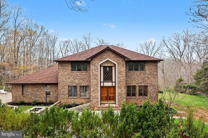 Tucked away in the prestigious Cathedral Forest community of Fairfax Station, this extraordinary custom home is being offered for the very first time by its original owner. Privately situated on 6.6 wooded acres, the property offers breathtaking views, complete privacy, and the rare opportunity to enjoy the beauty of nature without the upkeep —deer and other woodland wildlife are often right outside your window.
From the moment you arrive, the home makes a grand impression with its stately presence, expansive front patio, wraparound driveway, and two-car garage. Step inside to a dramatic two-story foyer filled with natural light and an airy, open feel throughout. The main level is designed for both everyday living and elegant entertaining. Newly refinished hardwood floors flow throughout the space. Just off the foyer is a private office or optional main-level bedroom, conveniently located next to a full bath. The formal dining room opens seamlessly to the spacious living room, creating the perfect setting for hosting gatherings.
At the heart of the home is the beautiful kitchen, featuring custom cabinetry, a large eat-in area, and views of the surrounding trees. The adjacent family room is warm and inviting, centered around a stunning stone fireplace and filled with natural light. From the kitchen, step out onto the rear deck and take in the peaceful wooded views and serene setting. Upstairs, you’ll find four spacious, light-filled bedrooms. The expansive primary suite includes an additional sitting room that could easily serve as a private office, nursery, or retreat. Every bedroom offers generous space and beautiful natural light. The walkout lower level is unfinished, but the possibilities are endless. With high ceilings, a window, exterior door, and space already ideal for an additional recreation room with a fireplace, this level offers tremendous potential to create significant additional living space and value. The mature Cathedral Forest neighborhood is known for its privacy, established setting, and beautiful homes. While there is plenty of usable side yard space for outdoor enjoyment, the majority of the acreage is wooded—allowing you to enjoy the spectacular views and natural surroundings without the maintenance of open land. A truly special property offering privacy, scale, timeless design, and endless possibilities in one of Fairfax Station’s most desirable neighborhoods.