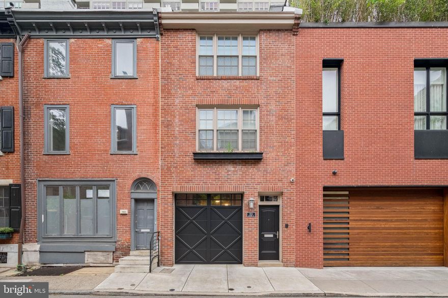 A crown jewel nestled in the heart of Philadelphia's most desired neighborhood, 1921 Manning St is a bespoke private residence just steps from Rittenhouse Square Park. This expertly constructed 3-story home offers 3 bedrooms, 3 full bathrooms, a sought-after 2-car garage, a peaceful terrace, a roof deck, and thoughtful details throughout. Lush trees line a quiet block, leading to the home's classic red brick facade with vibrant window boxes and black accents adding character. Stepping inside, the welcoming foyer makes an impressive first impression with gleaming tile floors, a built-in catchall shelf, and wainscotting along the wall. Ascending the unique dual staircase, you'll find a lavish main level that mirrors the pages of an architectural magazine. Soaring ceilings trimmed with crown molding and hardwood floors frame the open, airy space that takes full advantage of the home's extra deep lot. A set of tall windows brighten the inviting living room at the front. Past a powder room, a chandelier and wainscoting help define the center dining area, where there's plenty of space to entertain guests. At the rear is a showstopping gourmet kitchen adorned with high-end stainless steel appliances, custom white shaker-style cabinetry, black granite countertops, a tile backsplash, and an island with seating. Distinctive touches include a pot filler over the stove, double ranges, honed granite on the island, a wine rack, an appliance garage for hidden storage, and a dramatic tray ceiling. Off the kitchen, the serene terrace offers an escape from the city's hustle, perfect for barbecues and al-fresco dining, with a retractable awning acting as a shield from the weather. From the dining area, the dual staircase descends back down to the first level, which features a bonus room and full bathroom that could be used as a bedroom suite, den, or gym. There's also an entry from the 2-car garage and a rear patio. Up on the third level, the hotel-like primary suite has a large carpeted bedroom with two generous closets, lots of bright windows, and a raised section of the ceiling providing more light. The ensuite bathroom boasts a double vanity, a linen closet, and a glass-enclosed rainfall shower. Down the hall is a conveniently placed laundry room with a built-in ironing board, a full bathroom, and another spacious bedroom. Topping off the home is a pilot house with a wet bar and a roof deck that's the perfect spot to host friends and family or unwind with a glass of wine. Additional highlights include dual-zone HVAC, bull-nosed finished wall corners, and French doors with built-in blinds. 1921 Manning St is made perfect by its fantastic location, earning a Walk Score of 97! The city's best restaurants, shopping, and entertainment are all within a short stroll. There's also easy access to the Schuylkill River Trail, I-76, University City, Jefferson Hospital, and Pennsylvania Hospital. Plus, Rittenhouse Square Park is this home's backyard! Schedule your tour today.