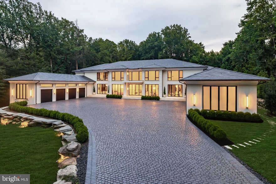 Rising above the rolling hills of McLean, Virginia, Bright Mountain Estate earns its name. Anchored by a sweeping boulder-clad drive and perched atop its own hill, the estate commands presence and privacy, an architectural summit overlooking 5.3 secluded acres. At more than 21,000 square feet, it is not simply a residence, but a landmark of design and ambition, brought to life by the visionary team behind Ambar. Seamlessly uniting bold contemporary architecture with timeless sophistication, it sets a new benchmark in McLean living and stands as one of the Capital Region’s most significant compounds.

A winding private drive unfolds into a grand approach, culminating in a broad motor court that underscores the estate’s commanding stature. The exterior, defined by concrete stucco, Vermont slate roofing, and copper detailing, conveys strength and permanence, softly illuminated in the evenings for a striking arrival.

Through towering glass doors, the entry hall reveals formal living and dining salons, each anchored by sleek floating fireplaces. Subtle architectural accents, including baseboard lighting, designer fixtures, and Lutron-controlled illumination, balance refinement with warmth.

At the center of the home, the great room rises to 28-foot vaulted ceilings. Walls of glass frame sweeping views of sculpted grounds, creating a dramatic yet inviting focal point. The adjoining chef’s kitchen, anchored by a La Cornue range, European cabinetry, and a Miele suite, is designed for both artistry and entertaining. A concealed spice kitchen expands functionality with additional prep space for seamless hosting.

The main-level primary suite captures the essence of a retreat. With tranquil garden views, a spa bath with a Victoria + Albert soaking tub, dual vanities, and bespoke dressing rooms with concealed storage, it evokes five-star accommodations. This level also offers a gentleman’s library, private study, and two powder rooms.

Upstairs, a second primary suite provides sanctuary with a fireplace-warmed sitting area opening to a terrace. Its ensuite bath features a shower room with six Riobel heads, while the dual-sided dressing room is lined with bespoke cabinetry. Four additional bedroom suites, each with private sitting areas and baths, complete the level.

The lower level transforms into an entertainment destination. A cinema with surround sound, a full wet bar, and a 3,000+ sqft recreation lounge offer space for gatherings. A glass-enclosed wine cellar doubles as art piece, discreetly concealing a safe room.

For the automobile connoisseur, the estate’s twin double-height garages are fully climate-controlled and lift-ready, accommodating eight vehicles with direct connection to the residence.

Outdoors, the estate extends its resort-inspired living. The heated marble-clad pool features a spa, tanning ledge, underwater seating, LED lighting, and a cascading waterfall with fire feature. A fire-pit lounge and climate-controlled pool house with Wolf fryer, retractable hood, fireplace, full bar, and heated cabana bath elevate outdoor entertaining year-round.

Behind the elegance lies uncompromising infrastructure. With 600 amps of power, six Carrier HVAC systems, dual instant Rheem water heaters, copper plumbing, a CAT generator, Honeywell security with 16 cameras, and full-home URC automation integrating sound, climate, and lighting, the estate blends modern efficiency with absolute reliability.

Just minutes from Tysons Corner and Washington, DC, Bright Mountain Estate is not merely a home, but a pinnacle. A landmark of vision, craftsmanship, and scale, it was conceived as a generational compound, destined to endure among the Capital Region’s most iconic addresses.