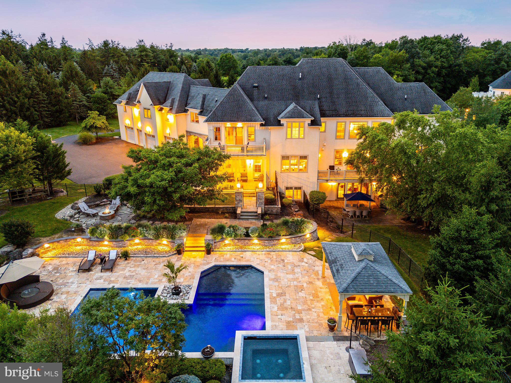 Welcome to 3 Stonebridge Crossing Road, an extraordinary estate offering privacy, elegance, and resort-style living in the heart of Newtown’s prestigious Creeks Bend community. Set on over 6 manicured acres, this custom-built residence combines timeless architectural design with modern amenities across 10,500+ square feet of refined interior space. Designed by the renowned Zaveta Custom Homes and envisioned by the esteemed Ralph C. Fey Architect, this six-bedroom, nine-bathroom residence stands as a true testament to luxury and refined living. Known for their exceptional craftsmanship and attention to detail, Zaveta and Fey have created a home that exemplifies elegance and sophistication. As you arrive, a sweeping drive leads through a professionally landscaped approach to an impressive motor court and porte-cochère, framed by a stately stone and stucco façade. A pair of handcrafted double doors opens into a dramatic two-story foyer with soaring windows, a sculptural floating staircase, and designer lighting. An elevator connects all floors, ensuring ease of access throughout the home. The main level features a formal dining room with abundant natural light, ideal for both intimate dinners and grand-scale entertaining. A richly appointed study with floor-to-ceiling wood built-ins offers the perfect setting for a private home office. The open-concept kitchen is a chef’s dream, anchored by a large center island, sleek stone countertops, and top-of-the-line Miele and Thermador appliances. A butler’s pantry with glass cabinetry and a beverage station seamlessly connects to the entertaining spaces. Adjacent to the kitchen, the sunroom flows into a comfortable great room with a linear fireplace and expansive views of the backyard. A secondary lounge area with large-format tile floors and custom built-ins offers flexibility for casual living or media viewing, while an additional sitting room with two-story ceilings and oversized windows creates a serene space for conversation or reading. Upstairs, the private quarters include five spacious bedrooms, each with direct access to a full bathroom. The luxurious primary suite is a true retreat, featuring French doors opening to a private balcony overlooking the grounds, a spa-style bath with an oversized soaking tub, dual vanities, custom storage, and generous closet space. The finished lower level is designed for elevated recreation and relaxation. It includes a stylish great room with a modern fireplace, a full wet bar with custom wine display, an additional office or executive workspace, a fitness room, and a playroom—all finished with high-end materials and thoughtful design. Outside, the estate transforms into a personal resort. The expansive backyard is centered around a beautifully designed pool with spa, water features, and an integrated sun shelf for lounging. A covered pavilion offers an elegant space for outdoor relaxation, while the built-in kitchen with stainless grill is ready for alfresco dining and weekend gatherings. A stone fire pit, multiple patio areas, and lush green lawns offer plenty of room for entertaining or unwinding. The grounds also include raised garden beds, a fenced play area, and carefully curated plantings for year-round beauty and privacy. Additional highlights include a spacious mudroom, four-car garage, recessed lighting throughout, wide-plank hardwood flooring, and multiple zones for heating and cooling. Every inch of this home has been thoughtfully crafted with the highest standards in mind. Located within the top-rated Council Rock School District and just minutes from Newtown Borough’s charming shops, dining, and cultural attractions, this is a rare opportunity to own one of Bucks County’s most exceptional homes. 3 Stonebridge Crossing Road is more than a residence, it’s a lifestyle.