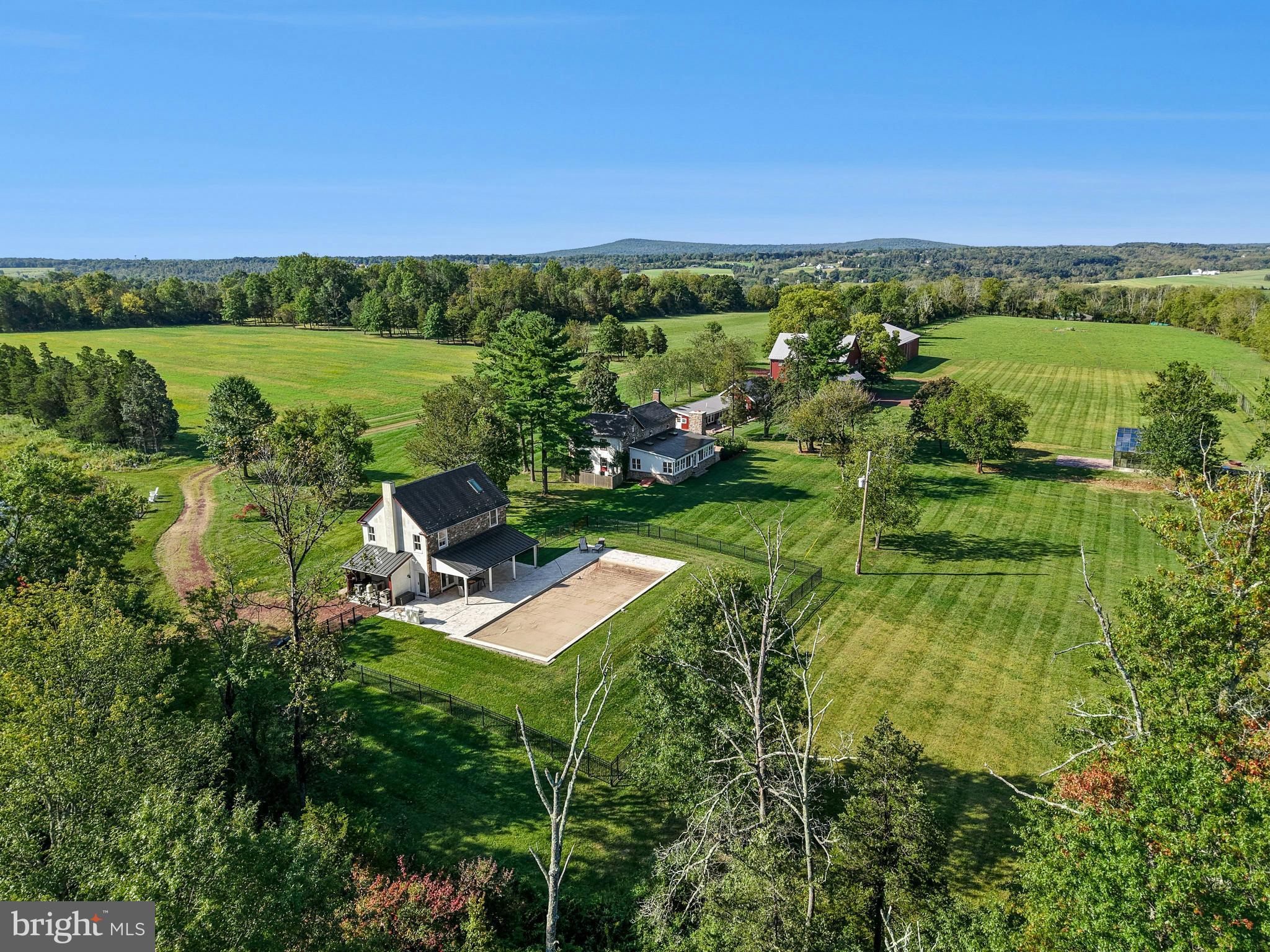 Bucks County farmhouses are defined by their settings and their position on their acreage, overlooking their fields and pastures, with long driveways leading past bank barns and farm buildings. Wheaton Fields Farm is one of the finest examples of these storied properties, boasting 50 acres of woods, fields, pond and even an orchard.
At Wheaton Fields, approach to the cluster of picturesque farm buildings is down a quarter mile drive, nicely removed from a quiet country road. The quintessential 1800’s pointed stone colonial, with rocking chair front porch, has been renovated and enhanced. A 2024 great room addition has three walls of glass, an exposed stone wall, wet bar, skylights, and fireplace, all opening to the sandstone patio with long distance views over the acreage and beyond. Pine, hickory and tile floors span both levels of the home. Throughout, 3 fireplaces, mullioned glass windows with deep windowsills, and period hardware attest to the classic Bucks County farmhouse character. Completing the first floor is a cozy living room with fireplace, dining room and charming country kitchen. On the second floor, there is an open and airy primary suite, bath and two additional bedrooms.
Outside, there are multiple buildings that have been cleverly converted into areas for guests, family, or hobbies. A picture-perfect 2017 pool house was designed to complete the original farmhouse with its own stone exterior. The stunning kitchen and great room with radiant heated floor opening to a covered patio and heated saltwater pool overlooking the orchard and greenhouse. Upstairs, a full bath and two additional studio rooms make this an ideal space for visitors. Nearby, one of the original farm buildings now boasts 3 charming cottages, 2.5 baths, as well as a family room, kitchen and laundry facilities. The three story bank barn includes a wing that has been converted into a studio, with bath and kitchenette. The 2015 pole barn will store every toy and farm essential and has solar panels sufficient to run the whole property. The private pond and dock beckon an afternoon on the water. Finally, there is a greenhouse and a fenced orchard with mature apple, pear, peach and plum trees.
This solar-powered property with generator lets you relax and invite a crowd for summer weekends, winter escapes, and every holiday. Whether a full-time residence or a weekend retreat, special occasions and other outside events will be celebrated here with joy. The views from the porch and patios provide an ever-changing panorama of seasonal colors and simple evening relaxation under the stars.
Wheaton Fields is the perfect farm property, enhanced by elements from a bygone era and nestled in a secluded Bucks County setting. This clever design allows for use as a family compound or for multi-generational living. This private paradise loses touch with the world just over the hills, yet is still within easy driving distance to magic weekends of Bucks County dining, antiquing and recreation. Estate appraisal of $3,150,000 available.