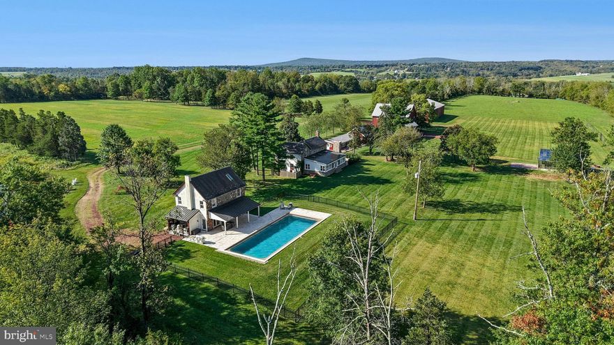 BUCKS COUNTY FARMHOUSES are defined by their settings and their position on their acreage, overlooking their fields and pastures, with long driveways leading past bank barns and farm buildings. Wheaton Fields Farm is one of the finest examples of these storied properties, boasting 50 ACRES OF WOODS, FIELDS, PASTURES and even an ORCHARD WITH GREENHOUSE.
At Wheaton Fields, approach to the cluster of picturesque farm buildings is down a quarter mile drive, nicely removed from a quiet country road. The quintessential 1800’s POINTED STONE COLONIAL, with rocking chair front porch, has been RENOVATED AND ENHANCED.  A 2024 GREAT ROOM ADDITION has three WALLS OF GLASS, an EXPOSED STONE WALL, WET BAR, SKYLIGHTS and FIREPLACE, all opening to the sandstone patio with LONG DISTANCE VIEWS over the acreage and beyond. Pine, hickory and tile floors span both levels of the home. Throughout, 3 fireplaces, mullioned glass windows with DEEP WINDOWSILLS and PERIOD HARDWARE attest to the classic Bucks County farmhouse character. Completing the first floor is a cozy living room with fireplace, dining room and charming country kitchen. On the second floor, there is an open and airy primary suite, bath and two additional bedrooms. 
Outside, there are multiple buildings that have been cleverly converted into areas for guests, family, or hobbies. A picture-perfect 2017 POOL HOUSE was designed to complete the original farmhouse with its own stone exterior. The stunning kitchen and great room with radiant heated floor opening to a covered patio and heated saltwater pool overlooking the orchard and greenhouse. Upstairs, a full bath and two additional studio rooms make this an ideal space for visitors. Nearby, one of the original farm buildings now boasts 3 CHARMING COTTAGE SPACES, 2.5 baths, as well as a family room, kitchen and laundry facilities. The ORIGINAL THREE STORY BANK BARN includes a wing that has been CONVERTED INTO A STUDIO, with bath and kitchenette. The 2015 POLE BARN will store every toy and farm essential and has solar panels sufficient to run the whole property. The PRIVATE POND AND DOCK beckon an afternoon on the water. Finally, there is a greenhouse and a fenced orchard with mature apple, pear, peach and plum trees.
This SOLAR POWERED PROPERTY WITH GENERATOR  lets you relax and invite a crowd for summer weekends, winter escapes, and every holiday. Whether a full-time residence or a weekend retreat, special occasions and other outside events will be celebrated here with joy. The views from the porch and patios provide an ever-changing panorama of seasonal colors and simple evening relaxation under the stars.
Wheaton Fields is the perfect farm property, enhanced by elements from a bygone era and nestled in a secluded Bucks County setting. This clever design allows for use as a FAMILY COMPOUND OR FOR MULTI-GENERATIONAL LIVING.  This private paradise loses touch with the world just over the hills, yet is still within easy driving distance to magic weekends of Bucks County dining, antiquing and recreation.  Estate appraisal of   $3,150,000  available.  Additional 6.7 Ac wooded lot available.