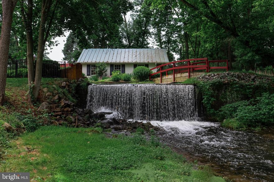 Nestled along the winding banks of Evitts Run, 6517 Kabletown Road, long known as Beeler’s/Clipp’s Mill, offers a rare chance to claim a remarkable piece of Jefferson County’s history. Dating back to the 1700s, this 3+ bedroom, 3.5 bath residence preserves its original mill water wheel and boasts ties to Civil War era events, blending historic authenticity with modern comfort.

The main level primary suite provides a private retreat, featuring vaulted ceilings, an ensuite bath with a soaking tub, and a sunroom with views of the rear patio. Upon entry, exposed logs and beams set a welcoming tone, while the updated kitchen pairs granite counters with custom cabinetry, a paneled refrigerator, and a wine “cellar.” The dining room’s original stone hearth stands as a centerpiece, honoring the home’s past.

A 2018 addition enhances the home while respecting its historic character. It includes a spacious family room or study with a propane fireplace, two offices, and a storage room, integrated so seamlessly they feel original to the property. Upstairs, two more bedroom suites each offer private baths, ensuring comfort for family and guests alike.

The rear patio provides a peaceful setting where waterfalls and the gentle flow of Evitts Run create a natural soundtrack. A charming footbridge crosses the creek, and nearly every room offers water views, transforming daily living into something extraordinary.

Completing the property are a detached two-car garage with workshop, a well house, shed, and gated entry. With its rich heritage, scenic surroundings, and enduring charm, this home is perfect for the preservation minded buyer seeking privacy, character, and a true sense of place.