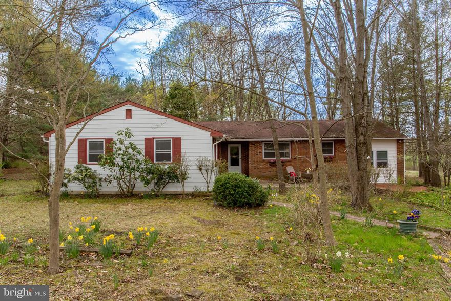 Located on a quiet country road in Solebury Township, this sweet ranch home is tucked away on over two park-like acres. With total privacy and country views from every window, this house is bursting with potential. A walkway leads to the front door where a bright foyer welcomes you inside. French doors open to the inviting living room with a wood burning fireplace and a swinging door to the formal dining room with chair rail. A sliding glass door ushers you out to the tiered deck with vaulted ceiling and screened-in porch, the perfect place to enjoy a cup of tea and watch the seasons change. The eat-in kitchen is warm and welcoming with granite countertops, tile floors, center island, and sunny breakfast room with exposed beams. Step down into the spacious den that spans the depth of the home and has a wet bar, bright windows, attic access, and a private entrance. The primary bedroom suite is generously sized with abundant windows and ensuite bathroom. Down the hall are three more well-sized bedrooms and a full hall bathroom with double vanity. The finished basement offers fantastic bonus space, clean dry storage with laundry facilities, and Bilco-style doors leading to the backyard. The gorgeous setting for this home is sure to impress with its flowering perennials and mature trees, while the expansive shady yard has abundant space for all your outdoor activities. Enjoy single level living conveniently located just minutes to New Hope, Peddler’s Village, and Doylestown.