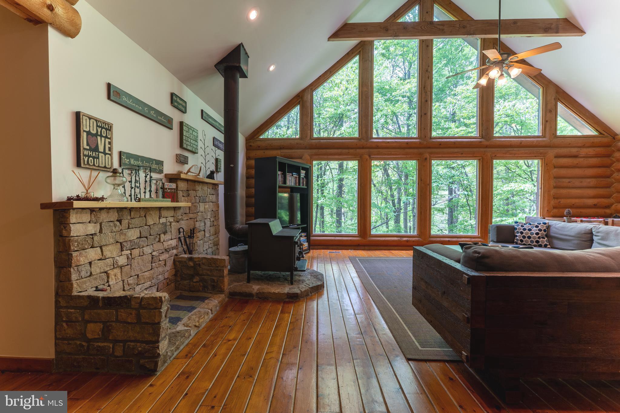 Tucked among towering pines and hardwoods, this fully TURN KEY 5-bedroom log chalet blends natural beauty with cozy, upscale charm. The home sits on a gentle slope overlooking a meandering stream, its melodic sounds carrying through the trees and adding a tranquil soundtrack to life. A wraparound deck offers views of the forest and stream bank. Inside, the open floor plan welcomes you with a grand sense of space. The heart of the home is a two-story great room, anchored by floor-to-ceiling windows bringing every bit of outside in. The stone setting of the woodstove radiates warmth and rustic elegance. Exposed 10" Western timber beams stretch across the vaulted ceiling.
The kitchen blends seamlessly into the main living area, featuring lighter wood cabinetry, granite countertops, and a large island perfect for gathering. An expansive dining area sits nearby with panoramic views of the forest.
The primary suite includes a private balcony, an ensuite bath with soaking tub and separate shower. Additional bedrooms offer ample space for family or guests.
A loft area above the great room provides extra living or workspace with an additional bedroom, while the walk-out basement includes a game room, 5th bedroom, 3rd full bath and access to a stone patio by the stream. With the roof replaced in 2023 and new furnace in 2021 and ac in 2024, no worries here! Move in and enjoy rental income or not! Just 6 minutes from Wisp Four Season Resort, 15 minutes to Deep Creek Lake State Park for beach, swimming and hiking and all shopping a can be found in McHenry, 6 minutes away. A perfect location for everything Garrett County offers. Buy now for summer rental income or to enjoy yourself!
