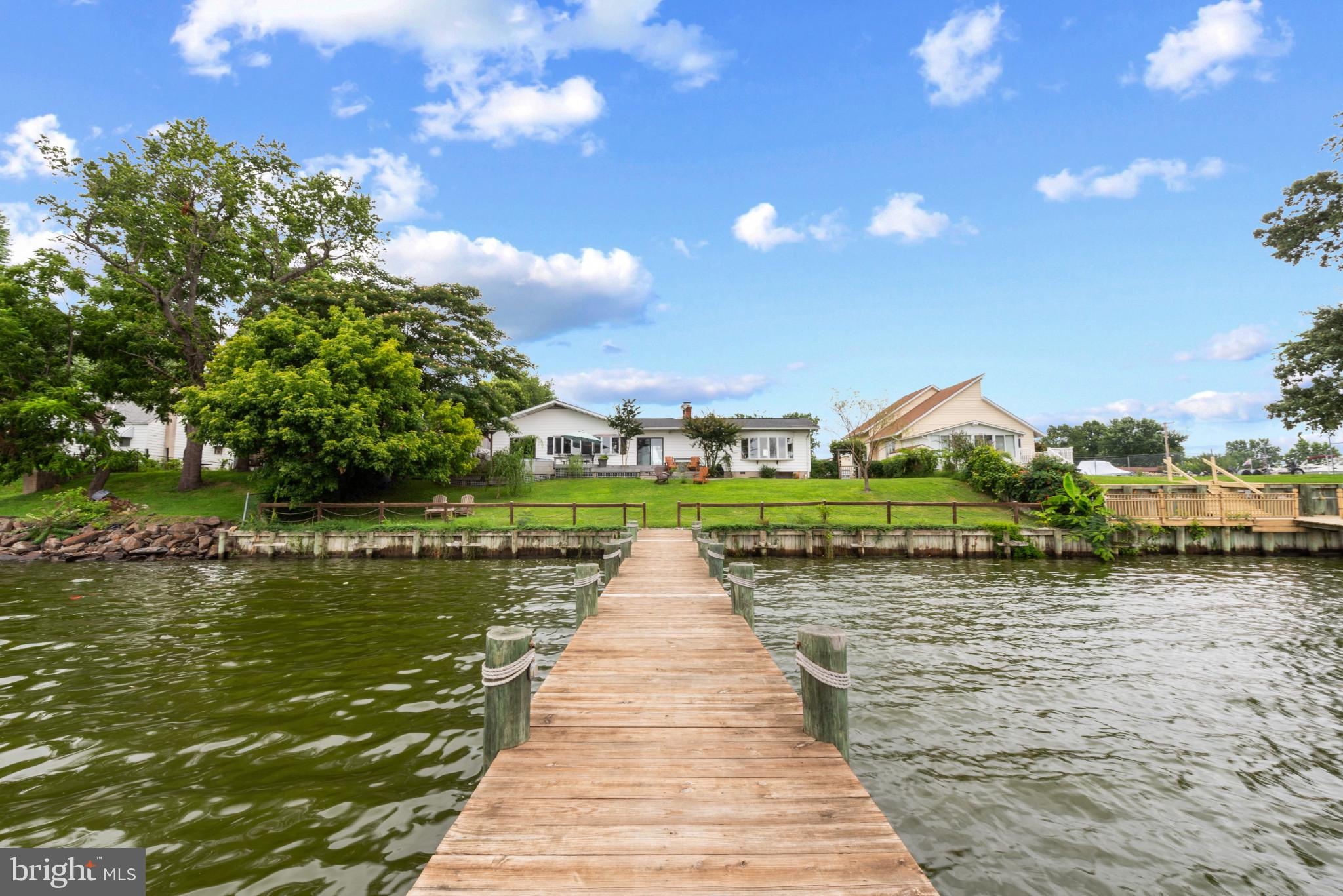 Welcome to your waterfront dream home! This stunning 5-bedroom, 3-bathroom rancher with a dedicated office/den and home gym offers luxurious single-level living right on the shores of the Back River leading to the Chesapeake Bay. Boasting expansive bay views, updated features, and private outdoor amenities, this home is a rare find.
Step through the elegant tile foyer and immediately feel at home. To your right, you’ll find a spacious den or office—perfect for remote work or creative pursuits. Turning left, the space opens up into a breathtaking riverfront kitchen, dining, and living area with panoramic water views. The open-concept kitchen overlooks Back River and flows effortlessly into the family room, where a two-sided glass wood-burning fireplace creates a cozy ambiance during colder months.
Dark bamboo flooring runs throughout much of the home, adding warmth and character. The primary suite is a true retreat, featuring a walk-in closet with custom barn doors, a beautiful spa-like bathroom with a soaking tub, and its own private sliding glass door leading to the back deck—perfect for enjoying morning coffee with uninterrupted views of the river. A built-in cabinet system and sitting area complete the primary bedroom.
Off the family room, you’ll discover a bright sunroom with more gorgeous water views and multiple sliding glass doors that lead to your private backyard, and a fully functioning hot tub that conveys with the property.
On the opposite wing of the home are four additional bedrooms. Bedroom 2 and Bedroom 3 are connected by a convenient Jack-and-Jill bathroom. Bedroom 4 is located near the rear of the home adjacent to the home gym, and Bedroom 5 is tucked quietly along the same hallway—ideal for guests or additional family members. A third full bathroom with a shower/tub combo is located just off the kitchen.
The home also features a spacious laundry room with pantry storage and access to the attic, which offers approximately 5–6 feet of standing room. This room also houses the water heater (replaced in 2014) and updated electrical panels.
Outside is your private waterfront oasis. A durable Trex deck spans the rear of the home, complemented by custom shutters made from repurposed wood. The new pier, built with extra height in 2014, includes one boat lift—capable of supporting up to 10,000 pounds—and three jet ski lifts that each support up to 3,000 pounds. All with electric and running water access. The home also features dual-zoned HVAC, new ductwork installed under the home in 2014, a newer AC unit (2014), and a roof also replaced in 2014. The crawl space offers additional storage and utility access.
Lush landscaping includes your very own peach and pear trees along the side of the home, and multiple outdoor hose hook-ups for convenience.
This one-of-a-kind riverfront property blends everyday comfort with waterfront luxury. Don’t miss your chance to experience life on the water at 520 Riverside Drive.