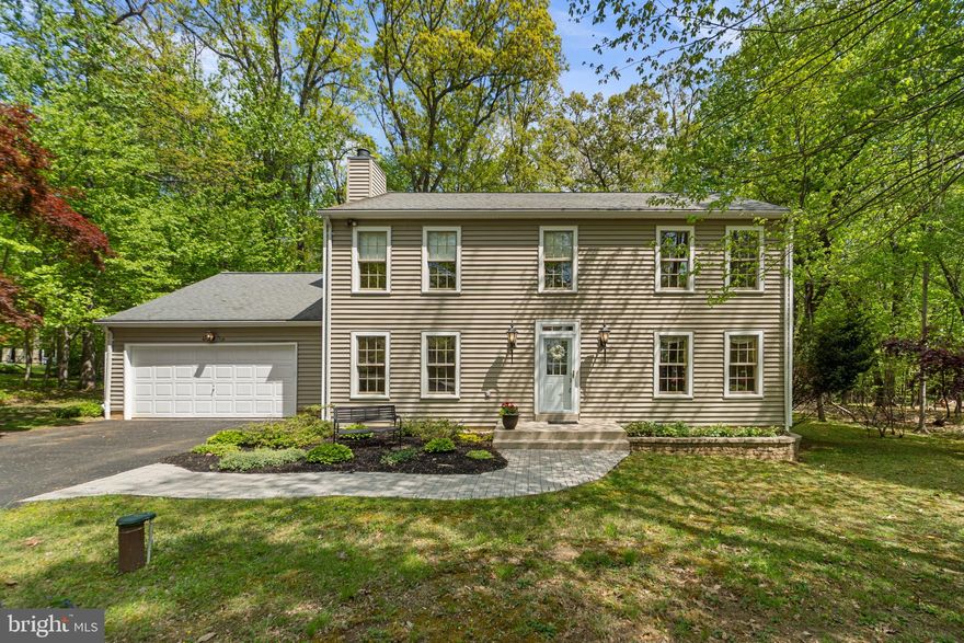 Charming Colonial residence nestled on a tranquil lot in Woodbine, offering 4 bedrooms, 2.5 bathrooms, 2,527 finished square feet, and a two-car garage on nearly a full acre surrounded by mature trees and natural scenery. // A brick walkway framed by lush landscaping welcomes you inside the traditional interior, where hardwood floors flow throughout the main level. Step into the bright, spacious foyer and continue into the formal living room, which transitions seamlessly into the elegant dining room. This space is full of character, featuring vintage-inspired wallpaper, rich lower wall detailing, and a sparkling chandelier. // On the opposite side of the foyer, a spacious family room provides additional living space, highlighted by a brick-accented wood-burning fireplace, built-in shelving, and recessed lighting—ideal for gathering, relaxing, or entertaining. // The kitchen features sleek black appliances, including double ovens, ample cabinetry and counter space, a custom backsplash with a decorative accent strip, two pantry closets, and an adjacent breakfast room filled with natural light. A powder room and laundry room add everyday convenience and complete the main level. // Upstairs, hardwood flooring continues throughout four generously sized bedrooms, including an expansive primary suite with a private ensuite bath. A second full bathroom serves the remaining bedrooms, one of which includes a walk-in closet for added storage. // The walk-up lower level offers a full basement space ready for customization or ideal for storage, providing excellent future potential. // Outdoor living is equally inviting with a patio overlooking a lush, tree-lined backyard that backs to woods—offering exceptional privacy, peace, and a serene natural setting perfect for relaxing or entertaining.