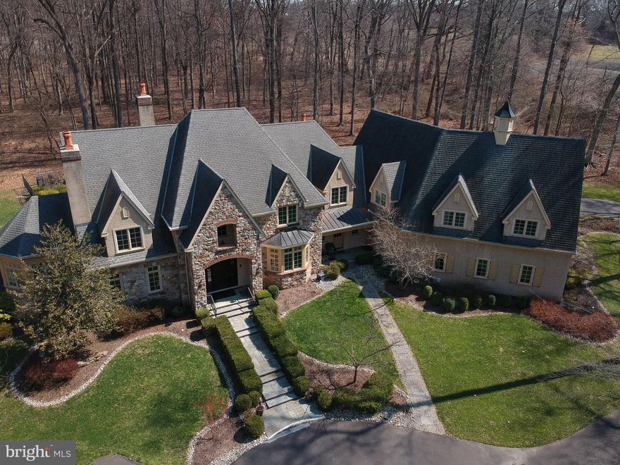 Surrounded by over 155 acres of permanently preserved land, 3525 Wellsford Lane offers something that cannot be replicated: total privacy, unobstructed views, and the certainty that the landscape will never change. Tucked within the exclusive Stoneymead enclave in Buckingham Township, this Trueblood-built French Colonial estate sits on 2.45 manicured acres bordered by 102 acres of conservation-protected Maximuck farmland, 45.8 acres of Buckingham Township preserved open space, and 7.86 acres of unbuildable Stoneymead common land. The setting feels like a private countryside retreat, yet you are just 90 minutes from Midtown Manhattan and minutes from Doylestown, New Hope, and Lambertville.
A circular driveway with fountain leads to the stone and frame facade. Inside, a two-story foyer with grand curved staircase opens to 10,000+ square feet of finished living space across three levels. Hardwood floors, custom millwork, crown moldings, and soaring ceilings set the tone throughout. LED lighting and a holiday candle window lighting package add warmth and efficiency. The two-story great room features a limestone gas fireplace, walnut built-ins, and a wall of windows framing the private grounds. French doors open to an expansive paver terrace with built-in Dacor grill and a heated Anthony Sylvan pool and spa with fountains and waterfall.
The gourmet kitchen is appointed with Wolf six-burner gas range with griddle, Wolf double ovens, warming drawer, Sub-Zero refrigerator/freezer, granite counters, and a center island with prep sink. A convenient laundry chute serves the upper level. A breakfast bar flows into the gathering room with cathedral ceiling, gas fireplace, and built-ins. The main level also includes a formal living room with gas fireplace and built-ins, formal dining room with tray ceiling and bay window, a study with wet bar and Sub-Zero refrigerator drawers, a butler’s pantry with Sub-Zero wine cooler, solarium with cathedral ceiling, laundry room, and a powder room at each end of the home. The oversized heated four-car garage features seamless resinous quartz flooring and a dedicated storage room. Built-in closets throughout the home provide exceptional organization and storage at every turn.
The upper level features five bedrooms and four full bathrooms. The primary suite is a true private oasis: a sitting room, his and hers bathrooms, dual walk-in closets with California Closets systems, and a private hallway creating complete separation from the rest of the home. The chandelier features a key-operated lowering mechanism for easy cleaning and bulb changes. A catwalk overlooking the great room connects to four additional bedrooms, all with California Closets; two are en suite and two share a hall bath. A walk-up attic provides generous walled storage space with potential to finish as an additional retreat.
The finished walk-out lower level adds approximately 3,500 square feet including a billiard room, exercise room, dance studio, granite-top bar and kitchenette, theater-ready media room, full bathroom, second laundry, and generous storage.
Since 2021, the owner has invested significantly in major systems: two new Trane central air conditioning systems (2021, 2022), a new high-efficiency Noble boiler (2022), a new Franklin submersible well pump with constant pressure controller (2025), new pool pump and start capacitor (2023, 2024), new pool cover, new sewer pump (2021) and ongoing HVAC maintenance. Five climate-control zones, whole-house sound system, central vacuum, security system, and indoor sprinkler system complete the package.
Award-winning Central Bucks School District (Cold Spring Elementary, Holicong Middle, CB East). Easy access to Routes 202, 413, and 611. A rare opportunity to own a truly private estate where the land around you is protected forever.