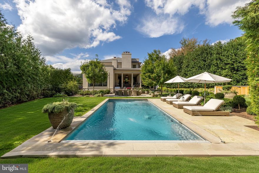 Nestled deep within a private enclave of distinguished residences just off Foxhall Road is 4849 Kemble Place, a custom Neo-Classic style residence designed by the award-winning architect, Anne Decker and beautifully constructed by Potomac Valley Builders.  Situated on a stunning 0.37-acre lot within a private peninsula, the property transports you to another place and time. This stunning home is approached by a broad set of limestone steps that lead to a charming columned portico and oversized front door that functions as a beautiful design element. Inside, the foyer has open sightlines to the public rooms. The grand staircase showcases white oak risers matching that of the elegant herringbone floors, beautifully contrasted with a dark gloss handrail. Formal living and dining rooms flank the reception area in a classic center hall configuration. The former, with a large bay window set against a wooded backdrop, is connected to the dignified library via French doors. The latter opens onto a spectacular loggia set amidst whimsical surroundings, blurring the lines between indoor and outdoor living. Anchoring the main level’s informal wing is the chef’s kitchen. Evoking a sophisticated European ethos, accent pieces include a custom stainless steel hood flanked by open glass shelving, all set against a large slab Carrara marble backsplash. A La Cornue range, inset custom cabinetry, Miele dishwasher, Waterworks fixtures, paneled wine and refrigerator columns, and a hidden pantry complete the space, which is truly a functional work of art. An adjacent, light-filled breakfast area offers an additional casual dining area. The family room's fresh-take on rustic built-ins and ceiling beams complement its roaring limestone fireplace to create a sensation of warmth. The windowed wall at the end of the family room paints a stunning picture of the pool terrace beyond. The grand staircase is illuminated by a pair of gridded skylights overhead, flooding the central well with natural light. The sumptuous primary bedroom features a dedicated sitting area, ceiling-mounted retractable television, and tastefully integrated cove lighting. The marble-clad ensuite bath comprises intricate mosaic flooring, double vanities, a freestanding tub with views, and a separate walk-in glass shower. Secondary bedrooms are each generously proportioned, painstakingly detailed, and luxuriously served by intricately tiled baths. Designed for the entertainer, the lower level comprises a large recreation room. A private bedroom suite with direct walkout access, an ample laundry room, as well as a mudroom area accessing the attached two-car garage complete the level. Perhaps the true highlight of this home is its outdoor spaces. A blend of manicured landscaping and extensive hardscaping has resulted in a space shrouded in total privacy by a verdant canopy. The side entry gate leads directly into an English garden running parallel to the loggia, which steps down to a central al fresco dining patio with a grilling area. The pool, nestled beneath a shimmering arch of water jets, is equipped with an automatic cover and lounging area. An additional side yard is stepped down, featuring a full turfed sports court.  Exquisitely finished both inside and out, convenient to Georgetown, Downtown, and major commuter routes, 4849 Kemble Place is an exemplary residence in one of DC’s most sought-after locations.