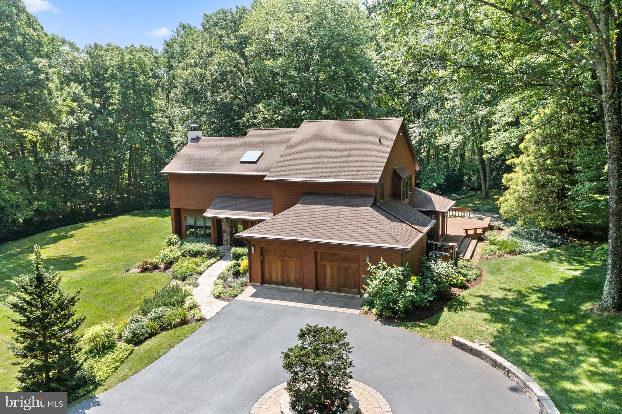 NEW PRICE!! Exquisite custom-built contemporary home nestled on 5.7 acres of serene and private land in the prestigious Radnor Hunt country. Beyond the gated entrance, a picturesque lane winds through lush landscaping, manicured lawns, and enchanting gardens, culminating in a circular driveway and a captivating stone-front home. As you step inside, a grand two-story foyer bathed in natural light from skylights extends a warm and inviting greeting. The living room, adorned with a striking stone fireplace, cozy window seats, and a sliding glass door opening to a delightful deck, offers an ideal space for indoor-outdoor living. Throughout the residence, stunning teak hardwood floors exude elegance and charm. An elegant formal dining room with a tray ceiling and recessed lighting seamlessly connects the living room, family room, and kitchen, creating a seamless flow for entertaining. The open-concept family room and kitchen boast a soaring vaulted ceiling with exposed wood beams, a two-story fireplace, a breakfast area, and a central island, perfect for gathering and culinary endeavors. A convenient mudroom/pantry with abundant storage and an additional sink leads to the attached two-car garage, providing practicality and organization. Ascending to the second floor, you'll discover a luxurious primary suite featuring a dressing area, a walk-in closet, and a spacious bath adorned with a generous shower and a soothing soaking tub. Begin your mornings with a cup of coffee on the private deck off the primary suite, reveling in the scenic views of lush landscapes and serene woodlands. The second floor also houses three additional bedrooms, a jack-and-jill bathroom, a hall bath, and a laundry room, ensuring comfort and convenience for all. Meticulously maintained, this exceptional home showcases an array of special features, including teak floors, skylights, intricate tile work, custom wood doors, and enchanting fireplaces. Spanning the rear and side of the house, a sprawling deck provides ample space for outdoor relaxation and entertainment, leading to a graceful blue stone patio, manicured lawns, and meticulously designed gardens. The property is adorned with spectacular woodland landscaping, creating a tranquil oasis for nature enthusiasts. Ideally situated in Malvern, this remarkable property enjoys the tranquility of a secluded lane while offering easy access to major routes, shopping destinations, renowned restaurants, and a plethora of amenities. Immerse yourself in the beauty and sophistication of this exceptional residence, where refined living and natural serenity converge in perfect harmony.