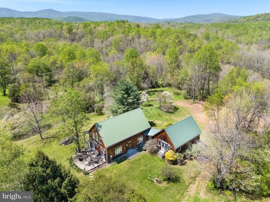 Frog Hill is the ultimate country retreat.   A cozy house, dramatic views, your own river to explore, and complete privacy.   Frog Hill has all this and more.  Barns for hobbies or livestock, garden areas to cultivate, and miles of trails to meander while enjoying the views and river frontage.  From every vantage point there is a masterpiece of nature to drink in.  Inside you can sit beside the cozy woodstove and watch the snow fall over the mountains in winter, or sit on the back porch to enjoy the summer breezes while the sun sets.

Residence
Built in the 1980s by accomplished woodworker, the house sits nestled amongst gardens and barn and two small outbuildings.  The simple structure is solidly built and features a soaring two story post and beam living room.  French doors lead to a patio with views.   The back porch also has excellent views.  The house has an efficiently engineered metal roof and cedar shake siding for low maintenance.

Lawns around the house are planted with specimen trees.  Spring bulbs (primarily daffodils) are underplanted along the house and at various focal points nearby.  There is a fenced kitchen garden with small garden shed with greenhouse attachment for potting and tool storage.  Specimen trees and shrubs surround the garden areas.

Open fields below the house afford 180 degree views of the Blue Ridge mountains from the Cobbler Mountains to the north to Mary’s Rock to the south.  There are outstanding and very private pastoral and mountain views in every direction.  Approximately 10 acres of open fields (no fencing) dotted with dogwoods lead down to woodlands that cascade down to the river.  Trails cut through the woods down to the river and to various granite cliffs above the river.   River frontage on the Rappahannock is nearly a mile in length.  The river frontage is an intensely private mix of swimming holes, granite cliffs, and gentle sandy bottomed river.  The river provides excellent fishing and is stocked by VA Fish and Wildlife.  Woodlands are a mix of tulip poplars (predominating), oak, hickory, virginia pine, dogwoods and redbuds.  A finer mix of views, river and privacy cannot be found anywhere else.