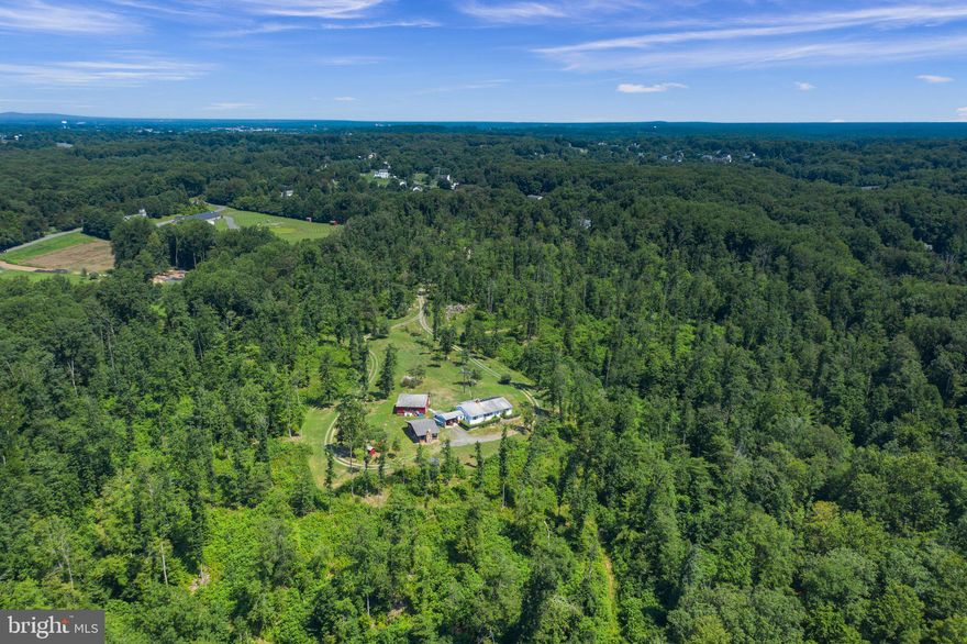 This property qualifies for Farm Credit financing, which is typically below market rates.  See DOCUMENTS. One of the last large parcels (46 acres) available in this highly desirable location. STUNNNING property. Enjoy the ¼ mile tree-lined private driveway that opens into a beautiful cleared area ready for whatever your imagination and dreams take you.  There are miles of well-maintained trails for hiking/jogging or just enjoying the abundance of wildlife and nature.  A babbling year-round stream adds the perfect touch. Or maybe your passion is 4-wheeling adventures.  Maybe you are looking for the perfect hunting property.  The range of uses are endless. It could be your own private oasis, a yoga/spa retreat?, multiple Airbnbs? Family compound? The house is currently occupied by the owners, and  Sellers are open to home inspection and consideration of repairs, but does need TLC..  The home is a quaint rancher with one master bedroom suite including full bathroom, and additional bedroom, also with full bathroom.  The existing den could be easily converted into a third spacious bedroom.  HIGHLIGHTS:  Outstanding views of the property and wildlife from the 3-season room.  ALSO HAS: two-sided fully functioning masonry fireplace which features woodburning stove in dining and fireplace in living room.  Huge windows in all rooms create outstanding views of the property and wildlife from the 3-season room is a bonus..  The outbuildings have great potential.  There is an original log cabin that is partially restored (love project or Airbnb?).  Cabin also has custom brand new windows ready to install.  The log cabin has existing electric service and plumbing hookup.  There is also a large work/barn with tons of space and includes a storage loft.  All of this and just 1 minute from Prince William Pkwy, and 2 miles from the new Harris Teeter grocery store, Starbucks, Giant, and Walmart.  There are no interior photos right now as the owners are in middle of boxing, storing in PODS, and typical moving disarray.  Previously under contract, but buyers did not perform.  Their loss, you new opportunity!