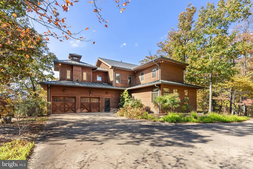 This unique property is the definition of an oasis in the woods. Surrounded by 180 glorious private acres, this home dazzles with grandeur while blending natural elements that mesh with the environment. The handsome hunter green standing seam metal roof with matching accents against wood siding is the ideal look for this 4,166 square foot architectural marvel. Indoors, there’s a thoughtful combination of plank walls, hardwood floors, tile, wall treatments, wrought iron, and stone to augment the theme.

On the main level, the vaulted great room is a showstopper where dining and gathering spaces share a bank of windows overlooking a breathtaking view of the great outdoors. A floor to ceiling stone fireplace is a commanding feature of the family room. The gourmet kitchen, which connects to the space, features two walls of staggered height cabinets, giving you ample room for storage and prep, with panels covering the Sub-Zero refrigerator for a seamless look. Sleek granite counters go with the theme, and grace the matching island, which holds a commercial-style Viking stove and double oven plus overhead ventilation hood. Dine-in seating for four is a nice island bonus.

A sunken den down the hall provides a cozier space perfect for entertaining or relaxing and benefits from another stone fireplace, wet bar, and abundant windows. Two generously sized main-floor bedrooms add to the versatility of this home and share a decadent en suite bath. You’ll appreciate the gorgeous touches, luxury vanity and bathtub, large walk-in shower, private commode, and linen closet. A laundry room and
half-bath are also situated on this level, as well as access to the attached garage, and outdoor spaces.

Upstairs, you’ll find a suite with adjoining living quarters. Both offer ample space for furniture and desired extras, and one side includes a lovely sitting room featuring an opulent fireplace and hearth.  The rooms share a decadent full bath with a double vanity, soaking tub, doorless shower, and private commode. This floor also includes a media or entertainment room (or 5th bedroom), and a centrally located mini kitchen in the hallway alcove allows for storage of snacks and drinks.

Outdoors, a viewing tower stretching three stories (accessible from the first and second levels) allows you to enjoy mountain views, glimpse abundant wildlife, and contains spots for seating and outdoor dining. There’s also a backyard patio and fire pit area. With so much nature at your fingertips, you can meander through the woods and pause at the creek traversing part of the property. The home is for sale furnished, so it’s not only meticulously designed and curated, but quite literally move-in ready. Whether you deign to live here full-time or as a weekend retreat, this extraordinary home is ready for you now.