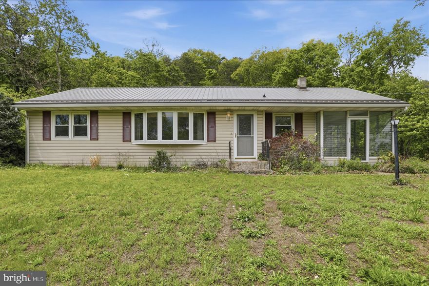 Welcome to The Hillside Ranch. Set back on 1.75 acres with a wooded backdrop just minutes from Cumberland, MD, this 1961 rancher offers the kind of setting that feels tucked away without sacrificing convenience. Affordable price with relatively low property taxes, this home presents an approachable ownership opportunity.

Inside, the home has been refreshed with clean, bright finishes while still holding onto its simple, functional layout. Hardwood floors run throughout. The updated kitchen features crisp white cabinetry, stainless steel appliances, and an easy flow into the adjacent dining area. With 3 bedrooms, 1 full bath, and one-level living, the layout is approachable, efficient, and comfortable. The bathroom has also been updated with a tiled shower and glass enclosure for a clean, modern finish.

Great for low-maintenance living, the home features a durable metal roof and double-hung vinyl replacement windows already in place.

The east/northeast-facing three-season room, featuring jalousie windows in excellent condition with optional screens, is a fantastic spot for morning coffee or tea.

Outside, the acreage opens the door for gardening, recreation, expansion, or simply more room to breathe. A generous detached garage adds storage flexibility while keeping vehicles protected from the weather.

A great ranch home in a desirable area with space, privacy, and updates already in place — ready for its next chapter.