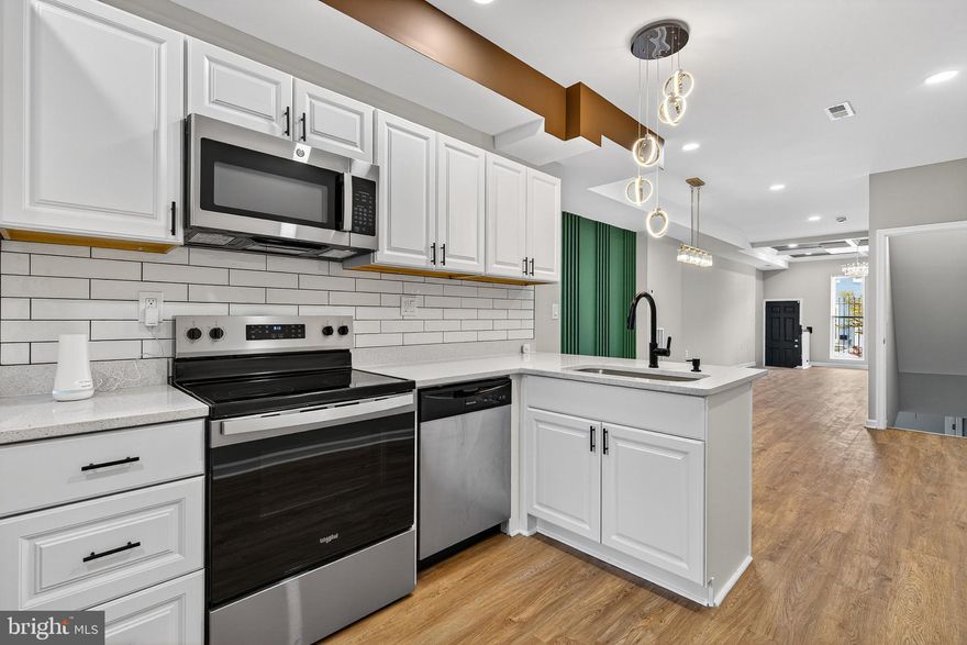 Welcome to 1912 Division St, a masterfully renovated townhouse that redefines urban luxury in the heart of Baltimore. This expansive 5-bedroom, 3-bathroom residence offers a seamless blend of contemporary architectural details and high-end finishes across multiple levels. Step into an open-concept main floor designed for both grand entertaining and comfortable living. The living area immediately impresses with its soaring coffered ceilings and a stunning tiered accent wall in a sophisticated slate grey. A designer crystal chandelier serves as the centerpiece, anchored by beautiful wide-plank flooring that flows throughout the home. The transition to the dining area is marked by a vibrant emerald-green feature wall with modern vertical slat detailing, illuminated by a contemporary gold-finished pendant light.
The heart of the home is a bright, professional-grade kitchen featuring: High-End Finishes, Sleek white shaker cabinetry accented with modern black hardware. Crisp white quartz countertops and a classic subway tile backsplash. A full suite of Frigidaire and GE appliances, including a French-door refrigerator with a built-in water dispenser. Striking circular pendant lights over the breakfast bar, perfect for casual morning coffee. The upper levels house spacious, sun-drenched bedrooms, each finished with plush carpeting and modern ceiling fans. The primary suite stands out with its custom wood-slat accent wall and a bold sage-green inset. Intricate marble-look porcelain wall tiles paired with unique pebble-stone shower floors. Gold-finished fixtures and framed mirrors that add a touch of elegance to the vanities. Contemporary grey vanities with integrated sinks and sleek matte black hardware. The finished lower level offers additional flexible space, ideal for a fifth bedroom, a private home office, or a media room. With every detail meticulously curated, from the recessed lighting to the minimalist trim, this home is truly a masterpiece of modern urban living. Experience the pinnacle of Baltimore renovation. Schedule your private tour of 1912 Division St today!
