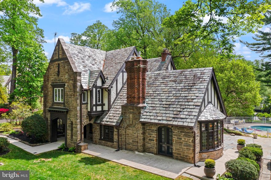 Welcome to Alden Manor. Upon the passing of Clement B. Newbold, his 350+ acre estate (Crosswicks) was sold for development. The architects (Wallace & Warner) were hired to design a series of classic country homes. This English Tudor constructed in 1933 retains so many of its original architectural elements. The original half-timbering & stucco is in exceptional condition, neatly detailed above the stone base. The slate roof retains the period appearance of its initial design. Many of the original leaded glass windows remain with unique stained & painted glass inserts. A covered entry provides protection from the elements at the front and a 2nd covered porch off the library provides space for outdoor entertaining in any weather. Enter the foyer and the original wide-plank pegged Walnut floors just shine! A grand staircase with wrought iron railings ascends to the 2nd floor. The spacious 19’ vaulted living room has beautiful cross beams, a large bay window with bench seating, a fireplace anchoring the front wall & French doors. Turn around to discover a delightful Juliet balcony upstairs. The large dining room faces the front yard and the courtyard garden with panel molding & a china closet. At the end of the foyer is the paneled library with a 2nd wood burning fireplace, the powder room and access to the covered patio. The eat-in kitchen is at the rear of the home that provides for direct access to the driveway as well as stairs to the 2nd floor and basement. There is an abundance of cabinetry and an island along with closets along the rear wall for coats and pantry items. As one ascends to the 2nd floor, there are multiple guest rooms anchored off the hallway. The primary suite spans the entire front of the house. There are two distinct rooms that are connected, each with their own en-suite bathrooms. One could combine these spaces to provide for a larger bathroom and/or a larger walk-in closet while still providing for two bathrooms for the owner’s suite. The lovely Juliet balcony is off the 2nd floor hall and there is a storage closet hidden next to the balcony. The next bedroom on this floor overlooks the side & rear yards and it shares a Jack & Jill bathroom with the next bedroom. This room is currently configured with walls of built-in bookcases and base cabinets in addition to the closet. From this bedroom, one has access to the rear staircase and to the final bedroom that is housed over the garage. That bedroom has its own ensuite bathroom. From the main hallway, there is a staircase to access the remaining living space on the 3rd floor. There are two more large bedrooms tucked up into the roof eaves, a full bathroom and a large storage area that houses one of the A/C systems. Down into the basement, there is a finished area under the living room with another fireplace that could make a great games room, gym or wine cellar. Under the dining room, foyer and library is the unfinished portion of the basement that houses the systems and provides an abundance of storage. Under the kitchen is the laundry room that is accessed from the rear staircase and there is a Bilco door that allows for the easy movement of furniture and other items. There is a large driveway that is accessed off of Kingsley Road, providing ample parking for at least 4 cars while the 2-car garage & side driveway provide additional parking options. There is so much more than meets the eye from the front of the home. With nearly 2 acres of private grounds, the majority of the land is behind the home. Off the side porch is a large patio that has the most unique custom granite picnic table & benches that can accommodate dinner parties of at least 16 people! The patio overlooks the inground pool. Behind flowering trees and shrubs is the tennis court! Still need more space, there is ample ground behind the driveway to add a sport court or simply a place to play catch or kick a soccer ball. Come explore Alden Manor, and maybe you can become its next steward!