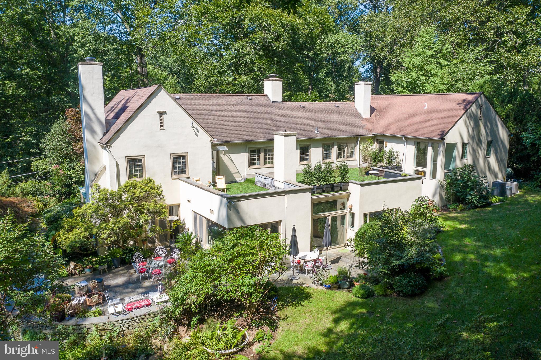 When the current owner first purchased 325 Millbank in 2002, the house and property, while lovely, needed some inspiration and imagination. First, the owner, an acclaimed landscape designer saw the redesign of the gardens. "Room after room" on the one (1) acre parcel were flowered, trellised, terraced, and enriched with a deep and exceptional variety of plantings with a rear yard of centennial trees providing a majestic backdrop and perfect opportunity to wind a secure walking path to Bryn Mawr college and back out into the world. The house, nestled within this sometimes formal, sometimes whimsical landscape has magic and appeal. Making sure to not squander the garden views or natural light that enliven the home, large format windows and full glass sliding doors were used at every opportunity, while richly stained hardwoods or painted tile floors add to the drama and elevated design. A double front entry leads to a step-down Living room/Dining room brightened by three exposures of light and warmed by a wood-burning fireplace. A wide cased opening connects to the Family room which also has a fireplace and beyond to an extraordinary eat-in kitchen with high ceilings, added in 2004 and inspired by the family love of cooking and gathering. All these spaces connect to bluestone patios, one with a fire-pit, with stone wall and large seated area, the other with a built-in gas grill and flat play yard. Fully custom curly maple cabinets, stone counters and an oversized seated island set the stage for highest quality appliances including an in-wall Miele coffee maker, Subzero refrigeration and Wolfe 6-burner gas cooktop and wall ovens. The performance of the kitchen design is outstanding and the feeling of welcome is tangible. One step away, find an oversized all-purpose room which functions as Butler's Pantry, Laundry room as well as extensive china storage; one step up is the coziest of den/libraries with brick surround fireplace and two full walls of shelving. The same wood crafter also saw to the kitchen desk, surrounding shelving as well as all built-ins in the mudroom/Family entrance. Ascend the front stairs to a light-filled and large master suite. The bedroom features a wood, turning fireplace and is spacious enough for additional seating and furniture. A fully outfitted large closet is accessed off the bedroom entry and offers plentiful walk-in as well as reach-in folding and hanging space. A double vanity bath with an independent tub and shower opens to a wide second level terrace with truly sweeping views of all of the rear yard spaces, gardens, and magnificent foliage. Two additional bedrooms each with bath are from the original 1938 structure while two large bedrooms with wide second level landing, purposed as an office, share a jack and jill bath with shower and tub. This home is truly more than the sum of its parts. The location is exceptional. The grounds are unmatched even when compared to those of arboretums and professional gardens and the house is at once practical, well laid out and yet warm, bright, welcoming and sophisticated