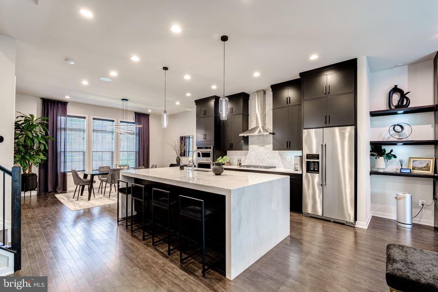 The seller is relocating, offering a rare opportunity—their loss is your gain! …….. Bring all offers!!

Welcome to 22158 Penelope Heights Terrace – Luxury, Location, and Lifestyle! The Towns at Metro Walk at Moorefield Station, where contemporary elegance meets convenience and style. This four-level simply stunning-L’Enfant model townhome, boasting over 3,000 square feet of thoughtfully designed space, offers the perfect blend of modern sophistication and everyday functionality.
Situated on a premium lot just minutes from the Silver Line Metro Station, this immaculate townhome offers over $100,000 in high-end upgrades and showcases true pride of ownership. Barely lived in by the original owner, the home is in pristine condition and move-in ready. **The seller is relocating, offering a rare opportunity—their loss is your gain!
This stunning 3 bedroom, 3 full bathroom, and 2 half bathroom home features elegant finishes, thoughtful design, and modern functionality throughout its four spacious levels.
Step inside to find smoke oak plank hardwood floors that flow throughout the entire home—no carpet to manage. The entry level offers a flexible space currently used as an office, complete with a full bathroom featuring white quartz countertops and mocha cabinetry, making it ideal as a guest suite or fourth bedroom. Just off the two-car garage is a custom drop zone with titanium granite countertops and mocha cabinets for added convenience and organization.
The heart of the home is the open-concept main level, perfect for entertaining and everyday living. The gourmet kitchen boasts high-end features including a stunning white marble waterfall island, under-cabinet storage, white marble countertops, a stylish white frost marble Chevron backsplash, a custom stainless hood canopy, KitchenAid stainless steel appliances, a sleek cooktop, and rich mocha cabinetry throughout. A generous walk-in pantry enhances your culinary experience.
The kitchen flows seamlessly into the dining area and the spacious family room, which is anchored by a show-stopping 64 in. LED Wall Mounted Electric black steel Dynasty Fireplace – encased in a floor-to-ceiling surround of Corso Italia Impero Black 12"x24" marble-look porcelain tile. Flanking the fireplace are thick black-painted pine wood shelves, adding custom warmth and style. From the family room, step out onto the covered porch featuring an outdoor gas fireplace—perfect for year-round enjoyment.
Throughout the home, you’ll find  smoke oak plank hardwood floors paired with oak stairs and upgraded wrought iron balusters, adding a touch of architectural elegance to every level.
Upstairs, the primary suite impresses with a large custom walk-in closet and a luxurious bathroom featuring a frameless glass shower with a rain head, dual sinks with Carrera white marble countertops, and upgraded designer tile. A second large bedroom with an en-suite bath features white quartz countertops and mocha cabinetry.  Plus, a spacious laundry room with granite countertops, built-in cabinetry, and a utility sink, complete this level. All bathrooms feature mocha cabinetry in keeping with the rest of the home’s design. 
The 4th level offers a versatile open loft with a second half bathroom, a wet bar featuring granite countertops, a KitchenAid beverage center wine fridge, and a sink. Access to a rooftop covered porch—complete with a gas rough-in for a fire pit or grill. This inviting outdoor space features Yardan Graphite 24" x 48" matte porcelain tiles and gray ABBA  patio tiles. Whether you're enjoying your morning coffee or evening cocktails, this rooftop terrace is the perfect place to relax.
Metro Walk offers resort-style amenities including a posh, modern clubhouse with a party room, a large outdoor pool, a fully equipped gym, yoga room, a playground, small office spaces and more!!