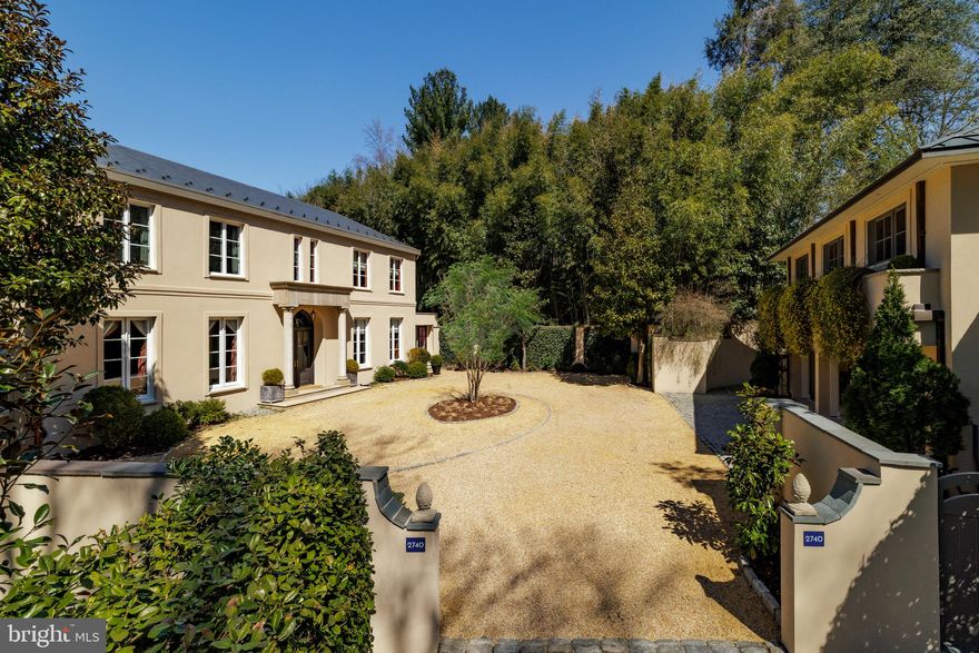 Branching off the prestigious Chain Bridge Road NW is a hidden private drive. The hedge-lined path meanders through verdant foliage to reveal a walled, circular pea gravel motor court upon which sits an elegant estate home. Evoking cues from the most vaunted European country homes, part Tuscan villa and part French provincial, the estate was created from the ground up by its visionary owner-developer. Constructed out of cinder block with thick walls and a recently refinished triple-coat stucco exterior, the home is a true fortress of luxury.

Stepping beneath the lofty portico and through arched double doors reveals the grand gallery, spanning the entire depth of the home. Hand-painted in a striking faux green finish by British artist Malcolm Robson to complement refinished herringbone floors, it sets the tone for the formal spaces. Soaring 11-foot ceilings, 8-foot solid mahogany doors, and elaborate P.E. Guérin hardware, including custom windows with crémone fittings, are testaments to the level of detail throughout.

The formal living room boasts custom plaster crown molding and an 18th-century French limestone fireplace mantle. Spanning 32 feet, it opens onto the rear terrace via twin sets of French doors. A 19th-century French marble fireplace mantle anchors the formal dining room, enhanced by mahogany paneling and Braquenié curtains in the La Rivière Enchantée pattern.

Recently expanded, the chef’s kitchen is divided into prep and cooking areas: one traditional, the other contemporary. Viking, Sub-Zero, Miele, and Gaggenau appliances represent top-of-the-line offerings, including six burners. A mahogany breakfast room completes the main level.

A vestibule leads to the upper-level primary wing. The bedroom features a raised pearl white ceiling and 18th-century Braquenié Le Grand Génois floral-patterned padded walls. The bath offers checkered marble floors, dual vanities, a jetted soaking tub, walk-in shower, and separate water closet. A wraparound dressing room with built-ins and track lighting completes the suite. Two additional ensuite bedrooms are uniquely styled.

The large lower-level recreation room opens through three sets of French doors to a parklike rear lawn. The exterior features a covered flagstone terrace, central lawn, al fresco dining area, and a custom stone pond set against a pergola with lattice fencing. Privacy is enhanced by a bamboo enclosure. A fourth bedroom with kitchenette and full bath can serve as a suite, with laundry and storage nearby.

HVAC systems include a 2023 Carrier unit for the main and lower levels, and a heat pump for the upper level. The hot water heater was replaced in 2024. A central vacuum system and new main-level glazing further enhance comfort.

Across the motor court is a separate carriage house with an inlaid cobblestone entrance, three-car garage, workshop, storage space, and trash room. Upstairs, the guest suite includes a kitchenette, full bath, living area, washer/dryer, dedicated HVAC, and private terrace.

Passionately designed, meticulously crafted, and situated in one of Washington’s most coveted enclaves, 2740 Chain Bridge Road NW is more than an estate, it is a masterwork of timeless European elegance and enduring architectural integrity. Rarely does a residence so completely embody privacy, provenance, and purpose. This is a home for the discerning few, a legacy property that will continue to inspire for generations to come.