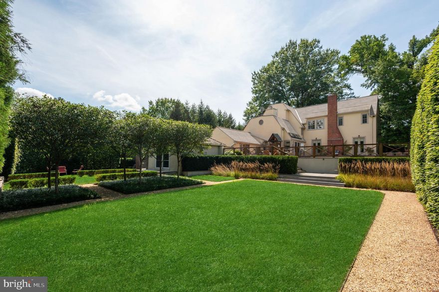 Synonymous with architectural charm and timeless appeal, the grand homes of Wesley Heights are among Washington’s most desirable. Within this verdant enclave lies 2927 44th Street NW, a European-inspired Tudor originally constructed in 1927. Perfectly sited just above street level on a private double corner lot of nearly half an acre, the residence combines historic character with thoughtful modern updates implemented beautifully by Solis Betancourt. A brick walkway meanders through the manicured front lawn, traversing a brick retaining wall upon which a neatly-trimmed row of hedges sits. The residence, with its gables, dormers, and cream stucco exterior, exudes the quintessential Tudor charm. The main entrance is located off a cozy brick patio beneath a petite portico, opening to reveal 5,100 square feet of ethereal interiors. The foyer introduces bright wood floors, sleek recessed lighting, and the grand staircase with an artful wrought iron baluster. Designed for large-scale entertaining, the formal living room spans 27 feet in depth and features a roaring wood burning fireplace framed by two sets of French doors elegantly opening onto the rear terrace to introduce an al fresco lifestyle. A sunroom is tucked away, with large picture windows overlooking the front grounds and a wall of built-ins for a quiet reading nook. Likewise, another sunroom is attached to the embassy-sized formal dining room, ideal as a private office. At the heart of the home’s informal wing is an open concept kitchen and family room. The former balances form and function with cathedral ceilings, granite counters, ample cabinetry, and top-of-the-line appliances from Thermador and SubZero. The latter features soaring vaulted and beamed ceilings with skylights, augmenting open sightlines to the rear patio via glass doors. A discreet wing contains a full main level bedroom suite. The upper level primary suite is entered via a dedicated vestibule within its own wing. A private sitting area is flooded with natural light. Ubiquitous luxuries include a gallery-like walk-in closet lined with built-ins and a marble bath with dual vanities, soaking tub, and heated towel rack for a sanctuary of comfort. Two additional bedrooms are located on the opposite side of the upper level, each with built-ins, expansive windows, and ensuite baths. On the loft level above is a fifth bedroom suite and attached bonus room. A sixth bedroom, ideal for an au pair or in-law suite, is found on the lower level in addition to a full bath and generous laundry room. A practical driveway runs along the side of the home, leading to the carport, motor court, and a detached room which serves as an exemplary fitness center, yoga studio, or zen space. Evoking cues of the Cotswolds with its yellow pebble paths and geometric greenery, the rear lawn, designed by Katia Goffin, was celebrated in Home & Design Magazine, exemplifying a seamless blend of hardscape and horticultural artistry. An elevated brick patio surrounds the heated lap pool, from which a sweeping view of the masterful grounds can be captured. Without peer in terms of location, the home is less than half a mile from Foxhall Square, 1.5 miles from the vibrant establishments of the Palisades’ main street, and just over two miles to Georgetown. Gracefully uniting timeless design, luxurious amenities, and extraordinary grounds, 2927 44th Street NW is a historic Tudor reimagined for modern living.