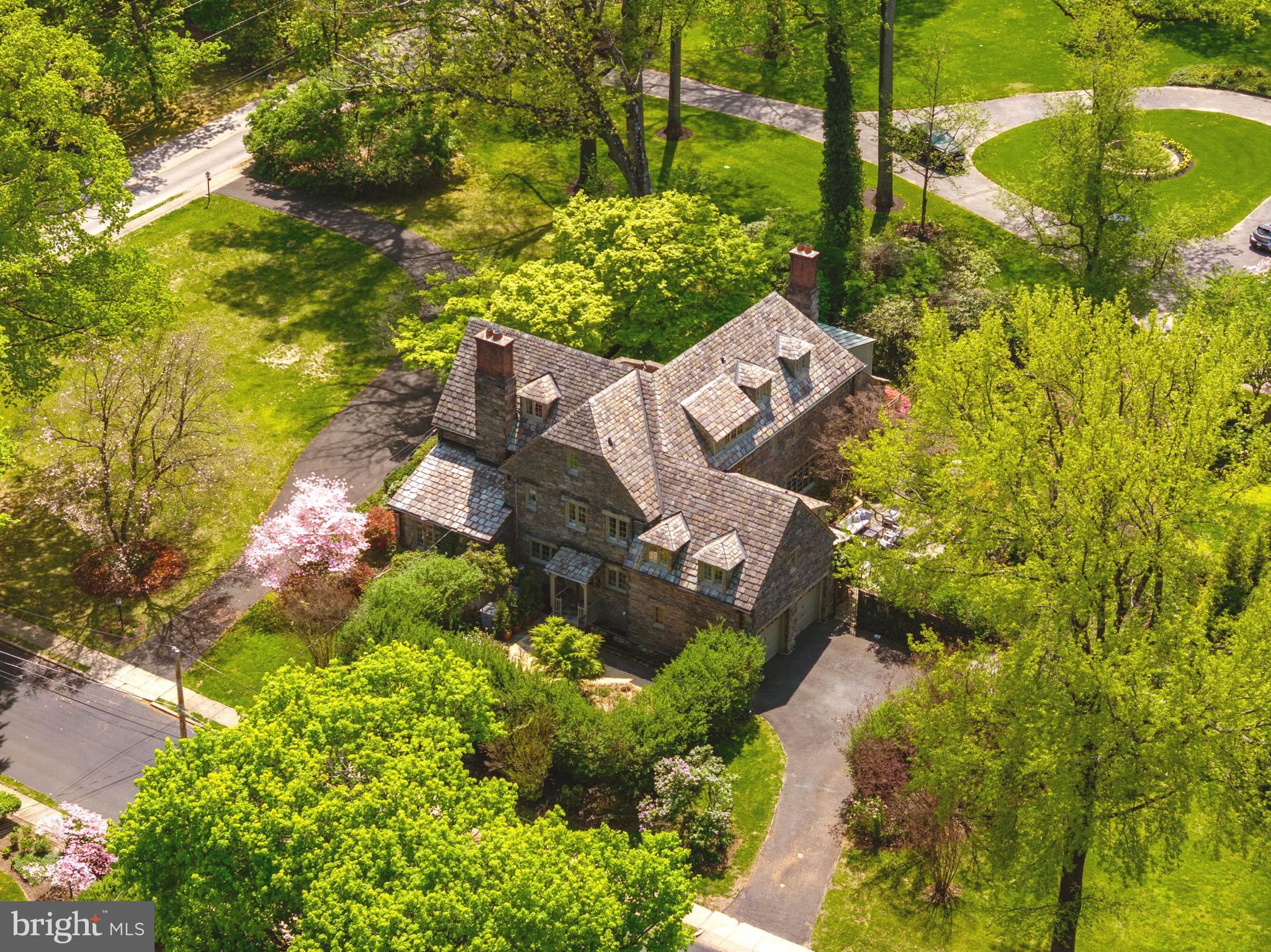 This classically designed and expertly constructed stone Tudor Revival masterpiece, built in 1928 by one of Philadelphia's most prestigious architects, Robert Rodes McGoodwin (also known for Chestnut Hill's 'French Village'), stands proudly today as a timeless treasure. Set on 1.05 acres in Elkins Park, on a beautiful tree filled block of Cedar Road, the home is surrounded by lush private gardens.
This architectural gem features remarkable details and exceptional craftsmanship at a level rarely seen. The current owners have maintained and updated the home impeccably, with over three hundred thousand in recent improvements. As you approach the stately residence via a large circular driveway, you are welcomed through a hidden stone entrance into the impressive grand center hall. The entry, with its soaring staircase and arched doorways leading to formal living and dining rooms, includes a half bath and a deep coat closet. To the left of the entrance, a few steps lead down into a gracious living room, which boasts walnut floors, a high-beamed ceiling, French doors, and a beautiful stone fireplace. The sun porch off the living room, featuring a flagstone floor and leaded glass windows, offers French doors overlooking the gardens. The formal dining room, with its marble fireplace, is perfect for gatherings, while the sunny breakfast room connecting the dining room and kitchen provides a cheerful atmosphere. The modern kitchen is spacious and includes a new induction cooktop, dishwasher, and refrigerator, marble floors, a mosaic tile backsplash, granite countertops, double ovens and microwave. Adjacent to the kitchen is a large renovated laundry room, a door leading outside to a small intimate garden, and a staircase to the basement, which offers ample storage and an outside entrance. The elegant staircase to the second floor leads to a large primary suite featuring a fireplace, a huge walk-in closet and additional large bi-fold closet. The primary bath has radiant flooring, a double vanity, and a walk-in shower. There are three additional bedrooms with a connecting full bath, and a half bath on this floor. One of the three bedrooms is currently utilized as a large family room, while another serves as an art studio. There is also a charming space designated as a quiet reading room with built-in bookcases. The third floor includes two more bedrooms, large closets, and a bath. Atypical of a 1928 build, this home offers an abundance of closet storage throughout, including two huge cedar closets on the third floor and another large hall closet on the second floor. Additionally, there is a spacious heated studio in the rear of the home, currently used as a pottery studio with a kiln. The home is equipped with three zones of heating and two zones of central air. The private gardens are a delight to explore. Close to the home, a large flagstone terrace is spacious enough for a dining table and lounge area, allowing for the enjoyment of the spectacular gardens. This area overlooks a lovely private garden room, with winding paths inviting you to wander further into the yard. An Asian-influenced garden room off the kitchen features a beautiful Japanese maple. Further from the house, there is a large grassy area surrounded by perennial beds, providing a constantly changing array of colors throughout the seasons. A back lounge area overlooks a small bocce court. This sale includes two separate parcels, with the second deeded lot fronting onto Sterling Road. The home is conveniently located just minutes from everything, including the charming Elkins Park with its restaurants and shops, the SEPTA Elkins Park train station, Target, Trader Joe’s, Whole Foods, shopping, additional restaurants, cafes, boutiques, schools, hospitals, parks, dog parks, trails, and golf courses. This location offers easy access to Wyncote, Jenkintown, Glenside, Abington, Huntingdon Valley, Mt. Airy, Chestnut Hill, Center City Philadelphia. Please watch beautiful Video