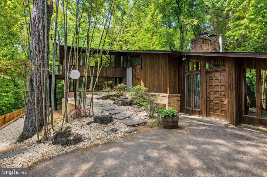 Tucked deep in the leafy quiet of Lake Barcroft Cloisters, this fully reimagined mid-century modern is one of the most architecturally distinctive homes to come to market in the community.
From the moment you arrive, the home announces itself differently — a zen-inspired entry garden of bamboo, river rock, flagstone, and flowering shrubs frames a striking dark wood facade with soaring rooflines and floor-to-ceiling black-framed windows. This is not a renovation. This is a reinvention.
Step inside to a breathtaking open great room where a vaulted wood-plank ceiling with exposed dark beams stretches the full length of the home — a signature mid-century architectural feature that floods the space with warmth and drama. Walls of glass and sliding doors open to a massive wraparound deck canopied by mature trees, blurring the line between inside and out. The chef's kitchen anchors the center of it all: a long quartz waterfall island, warm walnut cabinetry, professional range framed by matchbook-cut stone that mirrors the countertop slab, and a gorgeous deep blue subway tile backsplash that adds a rich, unexpected pop of color against the warm wood tones. Refined without being cold — every finish feels intentional.
The main level hosts two bedrooms including the private primary suite with walk-in closet and ensuite bath, joined by a second bedroom and full bath — ideal for guests or single-floor living. A family room, dining area, breakfast nook, and loft complete a main floor designed for both everyday living and effortless entertaining. An oversized deck connects you with the outdoors, giving plenty of space to entertain, dine al fresco, and enjoy the surrounding nature. The lower level features four additional bedrooms — including a generous room with its own walk-in closet — plus a large flex room, recreation room, two full baths, laundry, and dual utility rooms — space and flexibility for every lifestyle. Multigenerational living, home office suites, guest quarters — this floor handles it all without compromise. With 6 bedrooms, 4.5 baths, and 4,182 finished square feet across two thoughtfully designed floors on a private 0.42-acre lot, this home delivers scale, style, and soul in equal measure.