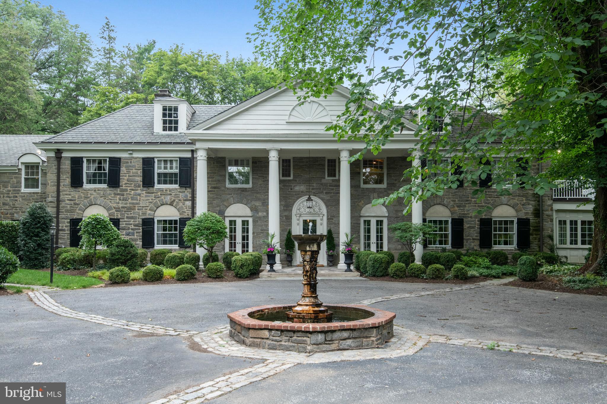 This Stunning Merion Golf Manor Estate embraces the rich architectural heritage of the Main Line. Meticulously and tastefully renovated to complement today's lifestyle, completed to the highest standards of the most discerning buyer. Offering high ceilings, walls of windows, and spectacular architectural details, the perfect marriage of luxurious renovations and original grandeur. A circular driveway with a whimsical fountain draws you to the columned entry of this Classic Stone Main Line Estate. Enter into an expansive and grand reception hall with a dramatic staircase. Beyond the center hall with a formal powder room, is the expansive living room with large windows and classic deep window sills, a fireplace with elegant marble surround, the perfect space to entertain in. Off of the living room is a sunroom overlooking the grounds with a fireplace, this space is currently a home office. Sliding barn doors lead you to the cozy family room with gas fireplace and custom built-ins creating the perfect place to relax or cozy up with a book. A Grand Formal Dining room also features an original marble surround fireplace and floor to ceiling windows and can accommodate large dinner parties. The show stopping Chef’s kitchen offers an intelligent design, eye catching designer accents and sumptuous finishes. The large seated island with Arabesque Marble Counter accommodates not only seating for five but a prep sink, GE profile refrigerator drawers, warming drawer, and ample cabinet storage. To name a few of the highlights the kitchen is graced with a 60 inch Wolf Dual Fuel Range, a 30” Subzero refrigerator, custom white cabinetry, two sinks for easy clean up - each with its own adjacent dishwasher and an ice maker in the beverage center. The kitchen has exposed beams in 3 places, a nod to the home's history, a stone accent wall with encased gas fireplace keeping it cozy all through the winter! A walk-in pantry, and a table with built-in bench seat for casual dining complete the space. Conveniently the kitchen is accessed by the second staircase leading you to the En Suite apartment above and offers access to the 3 car garage with 3 Tesla chargers. Off the kitchen a mudroom leads you to a breezeway with outdoor access to the powder room, and the expansive flagstone patio, the perfect place to enjoy outdoor dining or a coffee overlooking the grounds and gardens. Ascend the stunning staircase to the Primary Suite, truly a retreat, with marble surround fireplace, private balcony overlooking the grounds and an excellent vantage point of the tennis court, a large custom outfitted walk-in closet, and a luxurious spa-like bath. Recently completed, the Bath has a Copper Soaking Tub with jets that allows for two adults to fully submerge. Beautiful Ashford Carrara marble envelopes the bathroom and radiant heated floor, the hammered copper sinks complement the soaking tub, and the designer fixtures accent the bath and marble shower. Down the hall there are three en-suite bedrooms each with tastefully renovated designer bathrooms. A fifth bedroom is served by a full bath with a soaking tub accessed down the hallway. A fully renovated and self-contained apartment has its own kitchen, laundry rm, living rm, bed rm, and full bathroom, the perfect space for in-laws, or nanny suite with separate outdoor access. The Lower Level was recently fully renovated and offers a fireplace, a large screen TV projector perfect for movie night, a wood-finished wine room, powder room, and exercise room with rubber gym floor, and an additional storage space to complete the lower level. The over 2 acres of ground envelopes the Estate in privacy and the lighted tennis court delights in the spring, summer and fall months. There is a private gate that exits to Blakely for access for leisurely walks. This home also includes a central vac, tankless water heater, three zone HVAC, and surround sound. In the Heart of the Main Line & convenient to Philadelphia.