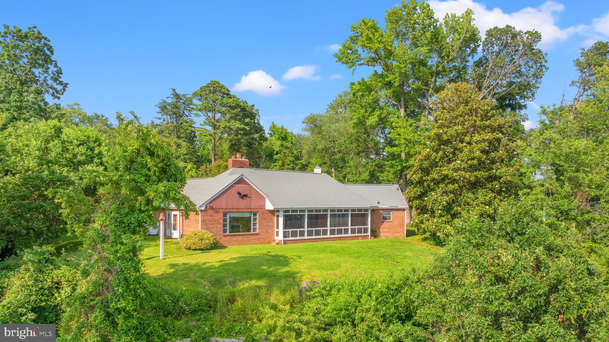 Nestled on 1.6 acres of serene, private waterfront, this charming farmhouse bungalow offers a true retreat from the pace of city life—while still being just 8 miles from Alexandria, 13 miles to Capitol Hill, and moments from National Harbor.
Tucked along the banks of Broad Creek with sweeping views of the Potomac River, this unique property invites you to relax and reconnect with nature. Whether it's quiet mornings watching herons and osprey from your screened brick porch, sunset reflections on the water, or weekend kayaking from your backyard, the possibilities for peaceful living are endless.
Inside, the home is steeped in vintage charm and warmth. Original woodwork, built-ins, and cozy fireplaces add character throughout. The spacious family room—anchored by a wood-burning fireplace and a wall of windows—boasts drop dead views year-round.
The main level features a spacious primary bedroom with a fireplace and water views, a second bedroom with private yard access, a full bath, and a kitchen with custom wood cabinetry, classic Thermador wall ovens and stainless steel appliances. Upstairs offers another bedroom, full bath, and a large high-ceilinged floored attic—that you can pop up to get picture perfect views of the water perfect for a primary bedroom/bath of your dreams.
Outside, enjoy brick garden paths, a walled courtyard with fountain, a roof cupola with weathervane, and lush landscaping—all adding to the timeless feel of this riverside hideaway. Need space for all your watercraft, bikes, and outdoor playthings - the attached 2 car garage it perfect.
This home was custom-designed and built by architect Dudley C. Bayliss, a renowned architect at the National Park Service from the 1930’s until 1966. Mr. Bayliss was instrumental in the creation of the Blue Ridge Parkway as both an architect and landscape architect. This home is full of custom features and detailed design elements quintessential in mid-century farmhouse style. No major renovations of this home have been undertaken in the last 50 years, preserving the style and distinct attributes of the original home.
This is a rare opportunity to own a sizable waterfront property with unmatched privacy and charm, all within an easy commute to the heart of the city.