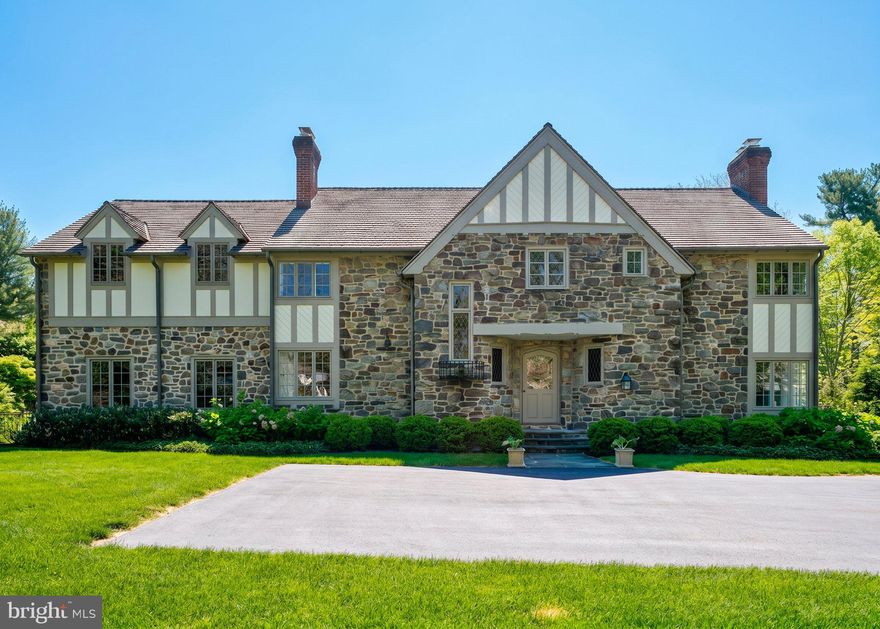 Set on the coveted north side of Bryn Mawr, this extraordinary Tudor revival is a masterful blend of timeless 1930s craftsmanship and sophisticated modern luxury. Meticulously restored and completely reimagined by Pinemar with design by Warren Claytor Architects, 617 Harriton Road is a one-of-a-kind residence offering over 3,800 square feet of beautifully curated living space in the award-winning Lower Merion School District. From the moment you arrive, the home’s architectural character is unforgettable. A striking exterior showcases hand-cut local stone, including rare touches of West Chester green serpentine and Wissahickon schist, creating a rich texture and presence rarely found today. The original oak front door with iron strap hinges opens into a gracious foyer where old-world charm meets refined contemporary living. Bathed in natural light throughout, the home’s flowing floor plan was designed for both elegant entertaining and everyday comfort. To the right, the dramatic formal living room features a soaring barrel ceiling and an ornate wood-burning fireplace that anchors the space with warmth and grandeur. French doors open directly to the terrace and grounds, creating seamless indoor-outdoor living. At the heart of the home is an exceptional chef’s kitchen, thoughtfully designed with custom cabinetry, quartz countertops, premium finishes, and an oversized island perfect for gathering. The adjoining family room and dining area create an effortless entertaining space, while expansive walls of windows and French doors frame views of the stunning outdoor setting. Step outside to the flagstone terrace and beautiful Paradigm pool, surrounded by lush landscaping and private lawn space that feels like a secluded retreat. One of the home’s most remarkable and unexpected features is the regulation-size Anderson squash court located just off the kitchen, a truly rare luxury. Whether used for squash, basketball, fitness training, yoga, pickleball practice, a wellness studio, or year-round recreation, this incredible space offers endless possibilities for all ages and lifestyles. A richly paneled library with custom built-ins and a charming corner fireplace provides the perfect setting for a home office, reading room, or intimate retreat. Throughout the first floor, impeccably maintained solid hardwood floors add warmth and authenticity. Original architectural details remain beautifully preserved, including solid wood interior doors, leaded diamond-motif windows, and wrought-iron Juliet balcony accents that subtly honor the home’s historic roots. The second floor is anchored by a luxurious primary suite featuring a spa-inspired bath with dual vanities, custom glass shower, water closet, and an oversized walk-in closet room. A private covered balcony offers a peaceful setting for morning coffee overlooking the beautifully landscaped grounds. Three additional bedrooms and a full bath provide flexibility for family, guests, or office space, while a conveniently located second-floor laundry adds modern practicality. Additional highlights include a new cedar shingle roof, whole-house generator, unfinished basement with perimeter drainage system, and countless thoughtful upgrades throughout. Ideally located within walking distance to Harriton House, the SEPTA Paoli/Thorndale Line train station, and the shops, dining, and amenities of the Village of Bryn Mawr, this turnkey residence offers an unmatched combination of architectural beauty, modern functionality, and premier Main Line living. 617 Harriton Road is more than a home... it is a rare opportunity to own a fully restored Tudor masterpiece with extraordinary amenities in one of the Main Line’s most desirable walkable neighborhoods.