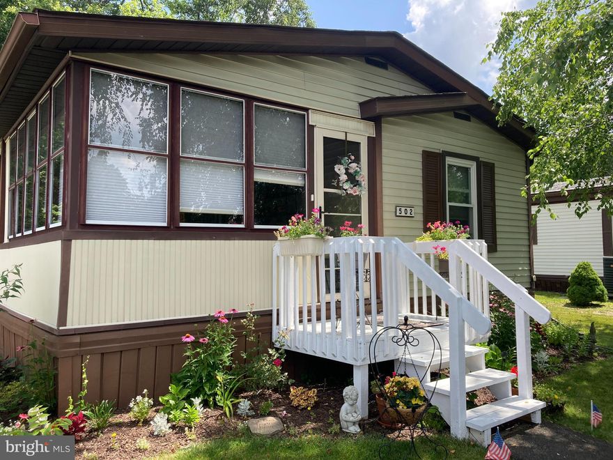 Come see this spacious Wayne model Neshaminy Falls 55+ home that backs up to a wooded area and comes with a grand room and high vaulted ceilings!  Park right in front of your beautifully landscaped home and walk a few steps into a roomy enclosed porch.  Marvel at the open-concept grand room with a conversation sitting area on one side and the other for TV watching and cozying up to a warm fireplace in the wintertime.  This huge space is also open to a newly renovated kitchen with newer cabinets and flooring and dining space that comes with the china cabinet.  Bedrooms are conveniently placed on opposite sides of the home for privacy when entertaining overnight guests.  The huge primary bedroom with new carpeting has an overhead fan, ensuite bathroom, vanity, walk-in closet, commode, and newer walk-in shower stall.  The guest bedroom is towards the front of the home with an overhead fan and closets.  The powder room is just off the living room and includes closets for even more storage.  This home comes with all-new windows, refrigerator, w/d, dishwasher, kitchen table and 2nd bedroom furniture.  Make your appointment soon!