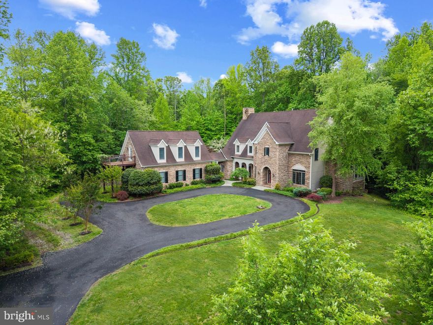 Experience timeless elegance and refined country living in this extraordinary 5BR/5BA/2HB estate, set on two private, wooded acres among multi-acre estates. Every element of this residence—from handcrafted woodwork to soaring ceilings and stone accents—evokes a sense of enduring quality and thoughtful design. The main level is a masterclass in warmth and sophistication, featuring rich wood floors, a grand stone fireplace, and expansive windows that frame tranquil views. The sunken living room invites conversation, while the formal dining room is ideal for hosting intimate dinners. A stately office with built-ins is the perfect place to catch up on some work and an unassuming bookcase near the powder room opens to a secret sunroom. Bathed in natural light and beckoning you to cozy up by the fireplace to enjoy the view, it’s a true retreat for quiet mornings or evenings. The heart of the home, the gourmet kitchen, is both elegant and functional—complete with a large island, walk-in pantry, breakfast nook, and a wet bar/coffee bar conveniently located between the kitchen and dining room. A spacious mudroom leads to a breezeway connecting the main home to a 3-car detached garage, topped by a luxurious guest apartment with full kitchen, living room, bedroom, bath, and laundry—perfect for extended family or visitors seeking privacy. Ascend to the upper level to discover a serene and spacious primary suite, featuring a peaceful sitting area, spa-like bath with soaking tub and oversized shower, and a generous walk-in closet. The upper level also includes a private guest suite and two additional bedrooms with a shared, thoughtfully appointed bath. The finished lower level offers exceptional lifestyle flexibility, with a sunken entertainment area, built-in wet bar, home gym, soothing fish tank, office/craft room, full bath, laundry and abundant storage. Outside, lush landscaping, a tranquil water feature, stone patio, pergola and al fresco dining area create a private oasis for relaxation and entertaining.  There is even potential for a stunning pool oasis, see rendering in Photos! This is more than a home—it’s a lifestyle of quiet luxury, just minutes from conveniences yet worlds away from the ordinary. Welcome Home!