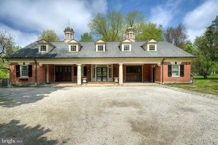 Tucked away on a quiet, tree-lined street in Chestnut Hill, this distinguished converted carriage house has been thoughtfully updated for modern living while retaining its original character. Originally built as the carriage house to a grand neighboring estate and converted in the 1980s, this 5-bedroom, 3.5-bath residence spans 6,000 sq ft on 1.36 acres and preserves many of its original details while functioning effortlessly for today’s lifestyle.

A long drive leads to a grand covered motor court opening to a welcoming foyer. The large first floor offers a well-designed floor plan perfect for entertaining and everyday living, with many original details throughout. The living room is defined by a dramatic two-story vaulted ceiling, oversized windows that fill the space with natural light, and a fireplace with a custom hearth anchoring the room, complemented by a wet bar tucked into a convenient adjoining entertaining nook. A powder room is located just off the entry.

The rear of the main level is dedicated to an open and expansive heart of the home, with the open-concept kitchen, great room, and dining area framed by three walls of windows and beamed ceilings. The kitchen is outfitted with a large island, a range with griddle, wok burner, and warming drawer, a Sub-Zero refrigerator, abundant cabinetry, and a double sink overlooking the walled side yard. The dining area opens to the rear deck through French doors, while the living area centers around an original brick hearth with a wood-burning stove.

The spacious and sunlit first-floor primary suite offers the ease of single-level living, complete with multiple closets and a spacious bath featuring double vanities, and a walk-in shower.

The upper level offers a rear bedroom distinguished by a graceful arched window overlooking the grounds, vaulted ceilings, and original built-in storage. An additional bedroom, a full hall bath with clawfoot tub, and a large walk-in closet complete this portion of the home. A separate suite provides exceptional flexibility, offering two additional bedrooms, an open living and dining area, laundry, a full bath with marble double vanity, and a kitchen with granite countertops, along with a separate entrance—perfect for in-laws or an au pair.

The expansive daylight lower level with laundry and walk-out access to the private, walled side yard and deck offers exceptional flexibility.

The home’s outdoor spaces are equally inviting, with a rear deck spanning the width of the home and steps leading to a side patio and lawn. The lush, fenced rear yard features mature trees and winding paths that pass through stone archways, along with a gate and stairs leading down to Springfield Avenue.

Ideally situated with easy access to local amenities, Fairmount Park and the Wissahickon, and just moments from Germantown Avenue, the home also offers a convenient commute via the St. Martins train station—creating a distinctive opportunity in one of Chestnut Hill’s most desirable settings.