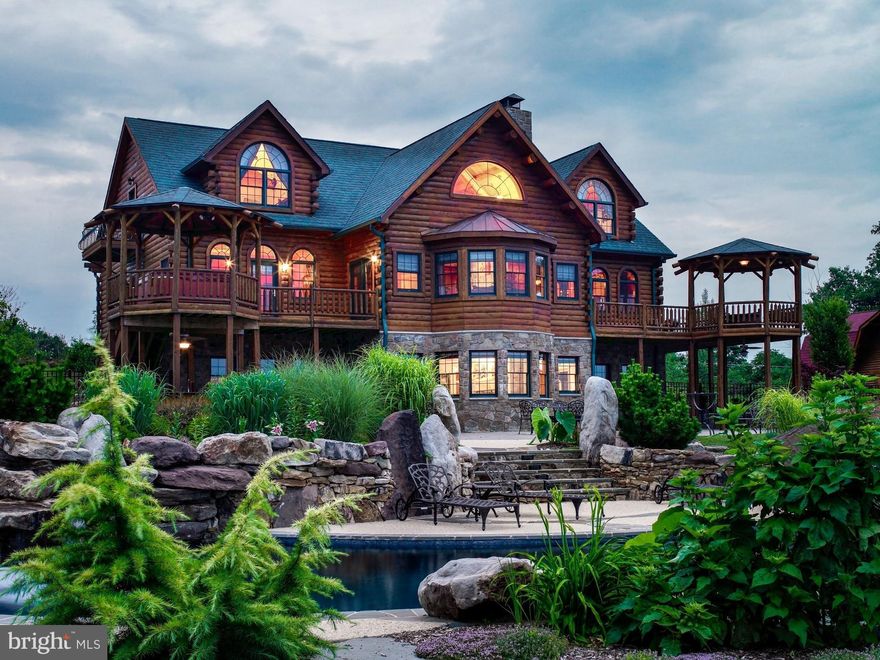 The majestic “Hennessey” log mansion, as featured in Country’s Best Log Homes’ article, appropriately entitled “Dream Fulfillment”, incorporates the best design elements from the most ambitious resort style homes.This stunning estate is harmoniously situated within a 5 acre bucolic setting among unique and mature specimen trees,landscaping, and gardens.Enter your grand home through the giant arched wood doors with wrought iron hinges and speakeasy window.The front doors, chimney, foundation, and other areas are accented by real stone,adding a certain rustic gravitas to the home.This stonework is mixed throughout the interior and exterior,a pleasant complement to the Northern White Cedar, and in perfect
balance with the solid walnut doors and carved wood mantels. You will be awe-struck as you stroll down the foyer and pass under the custom truss and beamed ceiling over the great room. The great room is flooded with natural light flowing through the fan window at the peak of the 24-foot cathedral ceiling. The great room’s bump-out is the perfect space for a cozy afternoon nap near the oversized fireplace. This alcove overlooks the vast backyard gardens, heated saltwater pool and waterfall,and an expansive patio.
Flanking the great room are the kitchen and dining rooms and the primary suite. The desirable first floor bedroom provides access to a walk out deck, gazebo and a hot tub to enjoy evening sunsets. This suite has a natural beamed ceiling and a noteworthy bathroom boasting a steam shower and a custom designed stonework tub surround. The first floor kitchen is easily accessed from the 3 car garage. The open kitchen has a large center island with a cooktop and plenty of counter space for socializing. The dining room features a stone fireplace and has French doors leading to a large deck and gazebo for outdoor entertaining with a view, or for a quiet evening around the firepit. Two bedrooms on the upper floor rival the size of the primary suite and include walkout balconies, giant arched windows, bathrooms and ample closet space. Each has intriguing ceiling designs and patterns in wood. Between the two bedrooms is a balcony sitting area overlooking the great room and a large open area leading to the private library, an indescribable architectural masterpiece with a cozy fireplace, balcony, and ample windows. The lower level is an entertainer’s paradise, including: a large main social and dance area with built-in bar and “cantina-style” seating, a temperature controlled 2000 bottle wine cellar, an extra large stone fireplace, and a theater area and billiard room with a beautiful stone alcove. Another comfortable bedroom and a similarly sized resting room and office adjoin the main room and bathroom. The lower level ties into an oversized fenced patio area and an outdoor kitchen and bar with underdeck drip proof seating areas. Stroll through the thoughtfully designed landscape to your koi pond, salt water pool, stone waterfall with hot tub. The layout is ideal for a large gathering or a secluded day under the shady wisteria-laced pergola. The yard area boasts 2 barns, greenhouse, fenced vegetable garden, and untypical trees in quality and quantity. Rare and stunning trees adjoin the neighboring forest reserve area providing additional privacy. The main barn has HVAC, water, electric, natural gas, and a full bathroom next to the gym area. The second floor lofts are bridged by an overlook with 1-ton hoist to the lower level. Four large 9ft tall drive-in doors allow for plentiful uses for contractors, auto buffs, woodworkers, landscapers, boaters, artists, and other craftsmen and hobbyists. You will be amazed by the charm and functionality of this building. The second log sided barn is two stories with electric, and water outside. Great for your tractors, animals or storage and nearby the newer greenhouse with power, electric and water. Feel like you're on a mountain vacation every time you step into your home!