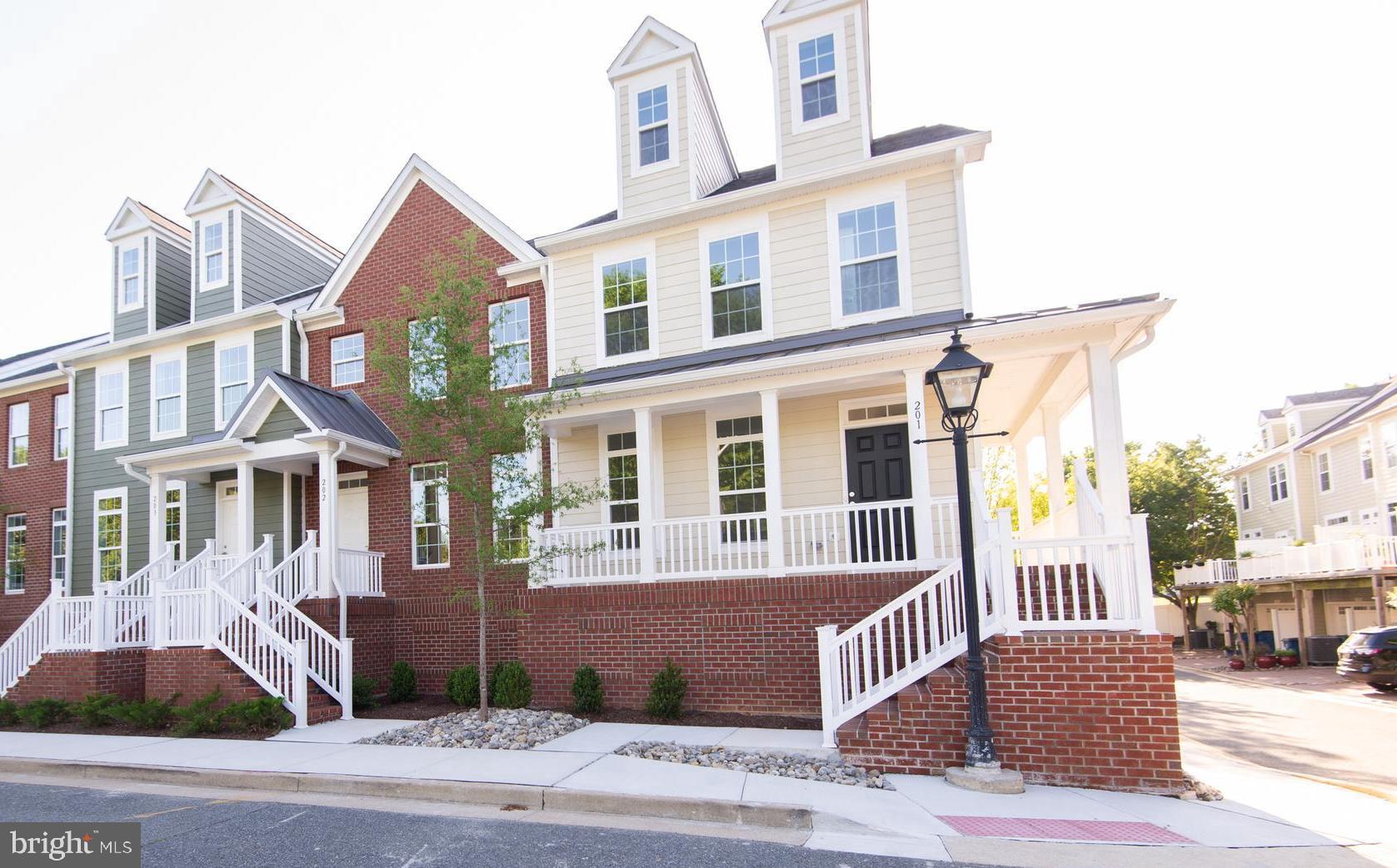 This newly constructed end-unit townhome at 300 Dixon Street offers a bright, spacious, and efficient four-level layout just a few blocks from downtown Easton. Finished in cream-colored Hardie Plank siding, the residence benefits from extra side windows that bathe the interior in natural light and a distinctive wrap-around porch—extending along both the front and side.
Level 1 – Garage & Service:
The ground level features a private garage with rear entry and direct access. This level also includes a half bath, a versatile bonus room, a dedicated laundry room, and a utility closet—ensuring everyday convenience and ample storage.
Level 2 – Main Living Area:
Step through a welcoming foyer into an open-concept space that seamlessly integrates the living room, a well-appointed kitchen, and an eat-in dining area. The kitchen is equipped with GE stainless steel appliances (cooktop, double wall oven, hood vent, dishwasher, refrigerator, and garbage disposal), complemented by upgraded quartz countertops and custom Timberlake cabinetry. Sliding glass doors lead to a balcony that fills the space with natural light, while a half bath, a coat closet, and a pantry round out the level. High ceilings, recessed lighting, and crown molding further enhance the inviting ambiance.
Level 3 – Bedrooms & Full Bathrooms:
Designed for comfort and privacy, the third level houses three bedrooms and two full bathrooms. Both full baths have been upgraded with quality Moen fixtures, glass shower doors, tile floors, quartz countertops, and custom Timberlake cabinetry, with white subway tiled showers. The primary bedroom suite features a generous walk-in closet and an expansive primary bathroom complete with a dual vanity and two storage closets for toiletries and linens. Carpeted bedrooms and hallways add a cozy touch throughout.
Level 4 – Loft:
The flexible loft, complete with its own mini split unit for heating and air conditioning, offers an adaptable space ideal for a home office, playroom, or additional living area. Abundant natural light makes this top level particularly inviting.
Community & Location:
Unit 201 is part of the Dixon Square Townhouses in Easton, located in Talbot County at the heart of Maryland’s Eastern Shore. The property is bordered by the nearly three-mile Easton Rails-to-Trails, offering recreational opportunities and convenient access to local shops, parks, and other destinations. Dixon Square itself features charming streetlights, brick stairways, sidewalks, and beautifully maintained landscaping managed by the HOA—making homeownership both enjoyable and low maintenance. Whether you’re drawn to outdoor adventures, the arts, festivals, or dining at a diverse mix of locally owned restaurants, this vibrant community provides endless opportunities to live your best life.